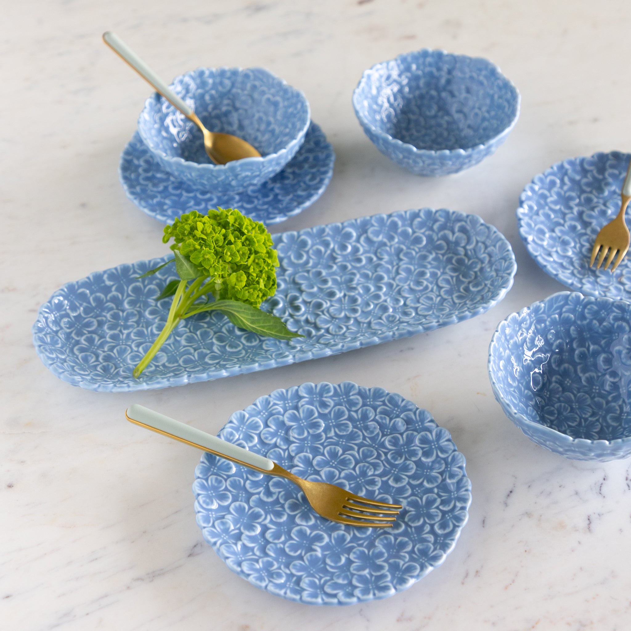Set of blue ceramic dishes with gold cutlery on a marble surface.