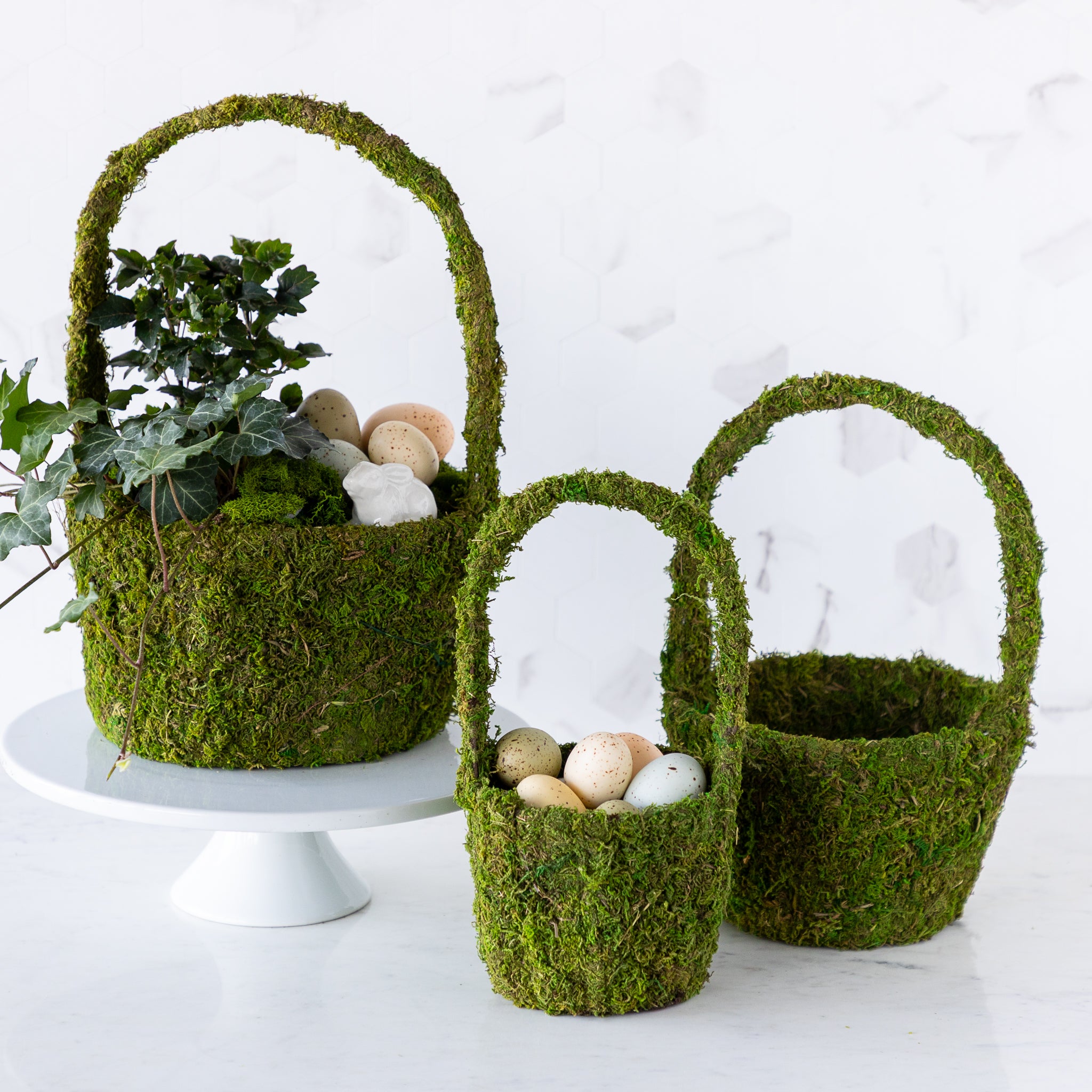 Three Decorative Moss Baskets: one showcasing a floral arrangement with plants and eggs, another filled solely with eggs, and an empty one, all crafted from preserved moss and elegantly arranged on a marble table.