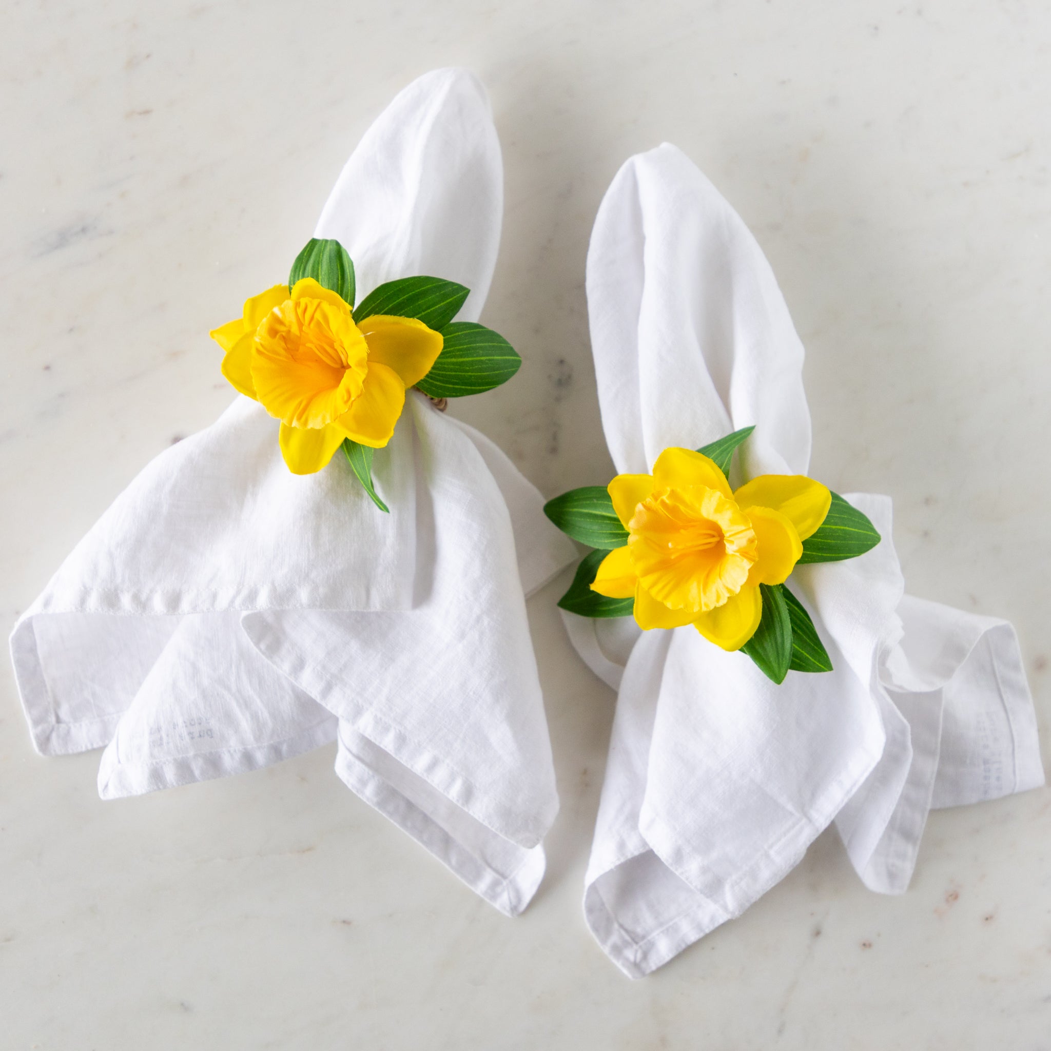 Daffodil Spray Napkin Ring Holders around two white linen napkins.