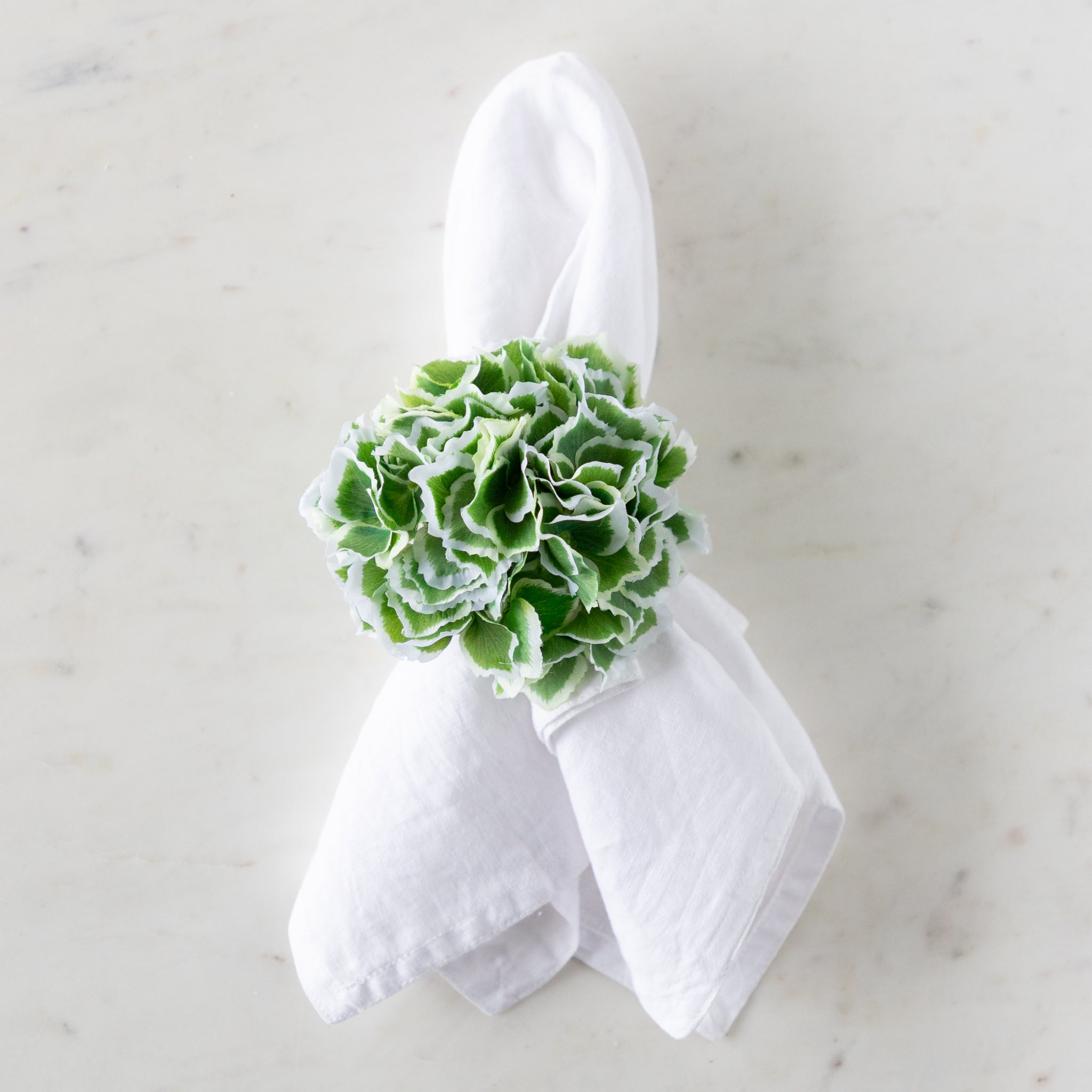 White napkin with a green Border Hydrangea Napkin Ring on a marble surface.