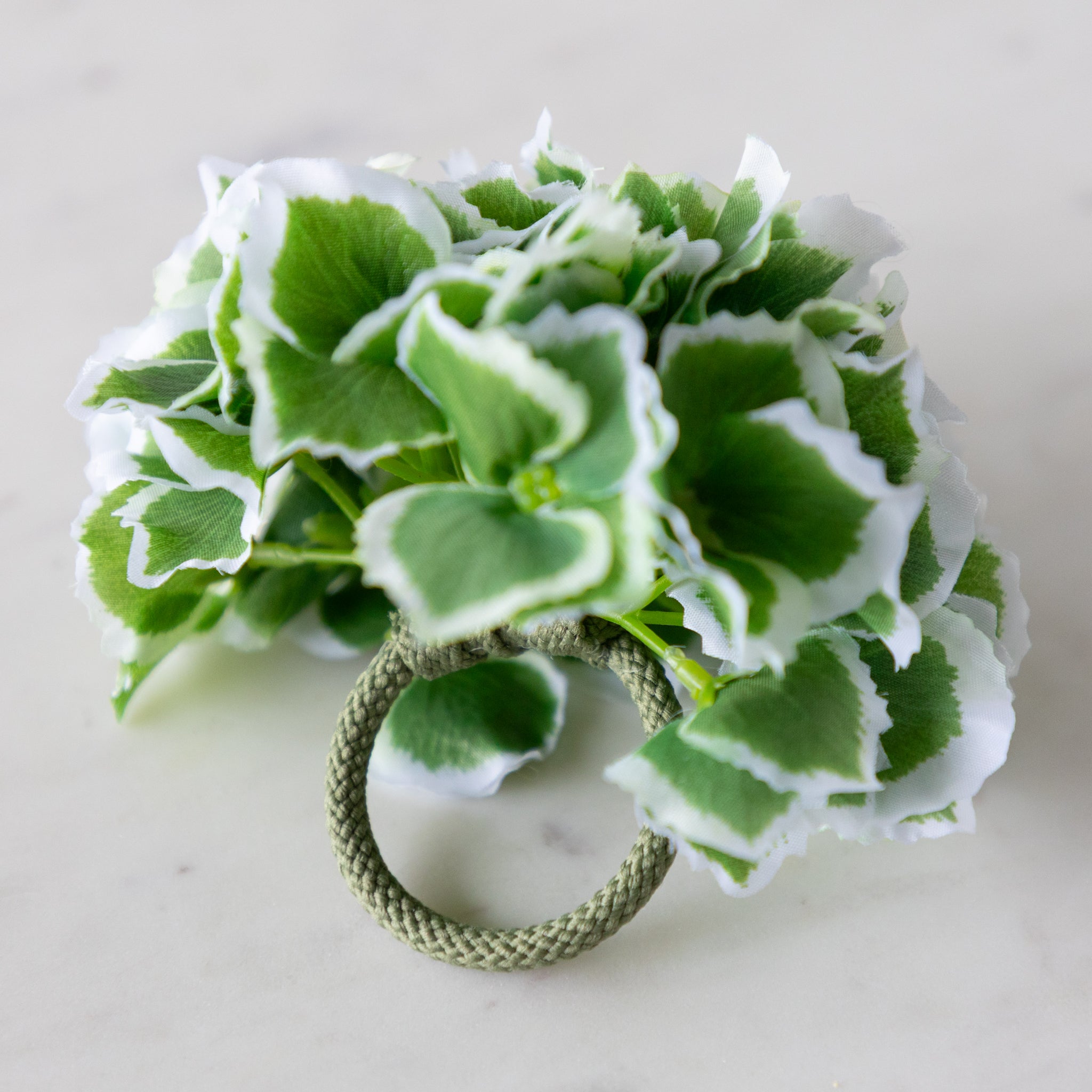 Green Border Hydrangea Napkin Ring with a green rope holder, on a marble surface.