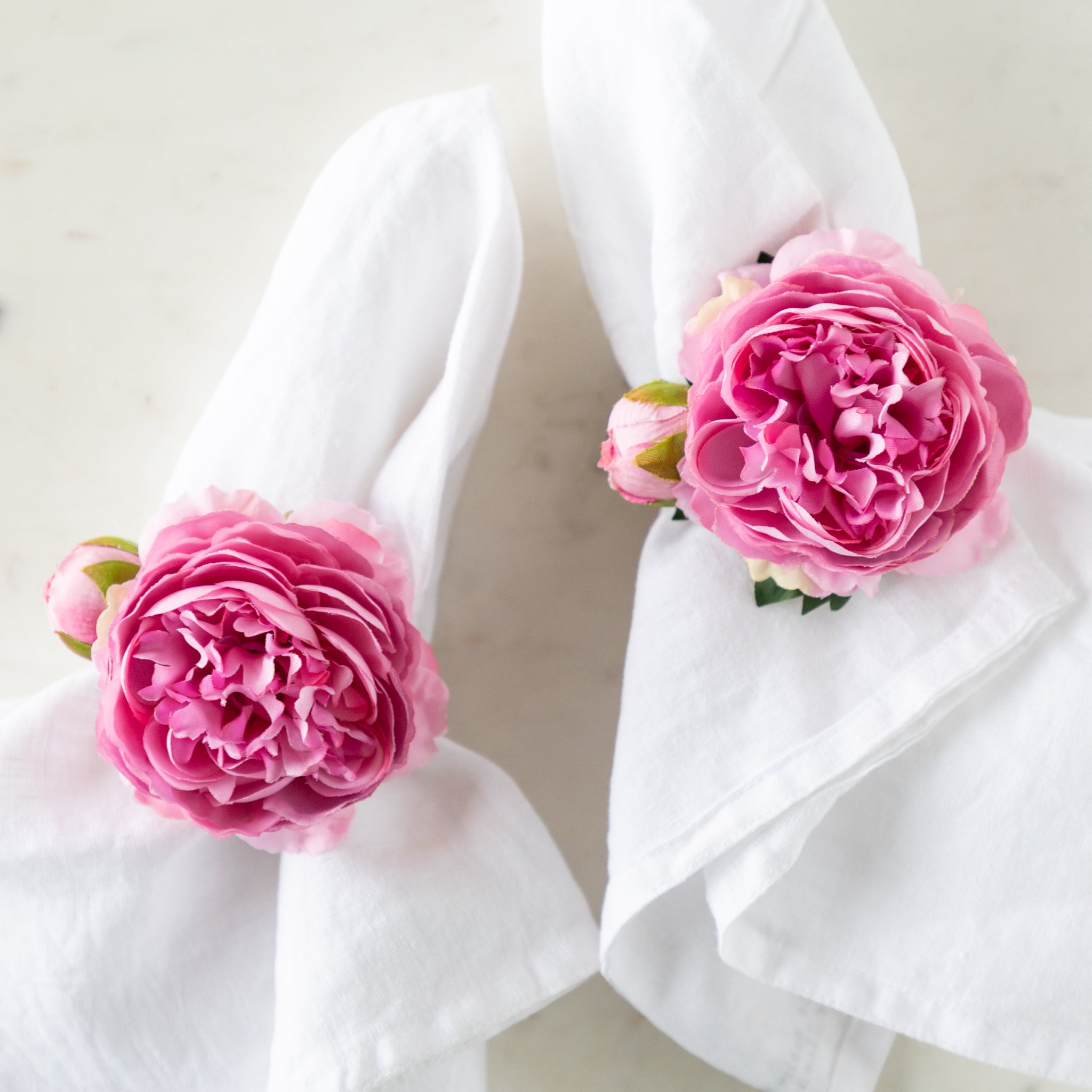 Pink Buttercup & Bud Napkin Rings around two white linen napkins.