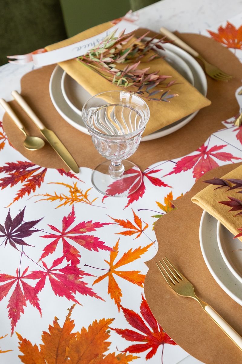 Thanksgiving table setting with fall leaf tablecloth, gold charger plates, and white plates.