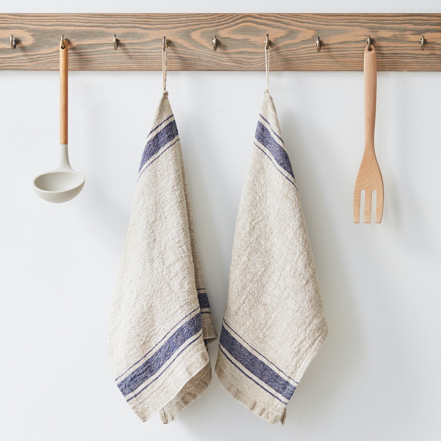 Two beige towels with blue stripes hanging on a wooden rack with kitchen utensils.
