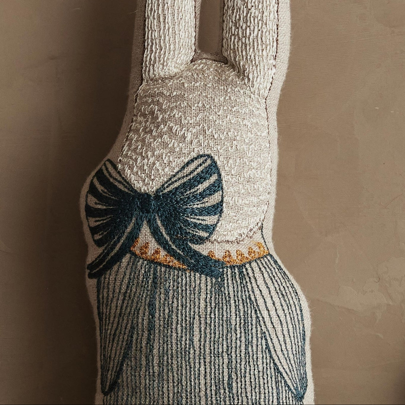 Plush rabbit-shaped object with a bow detail on a beige background.