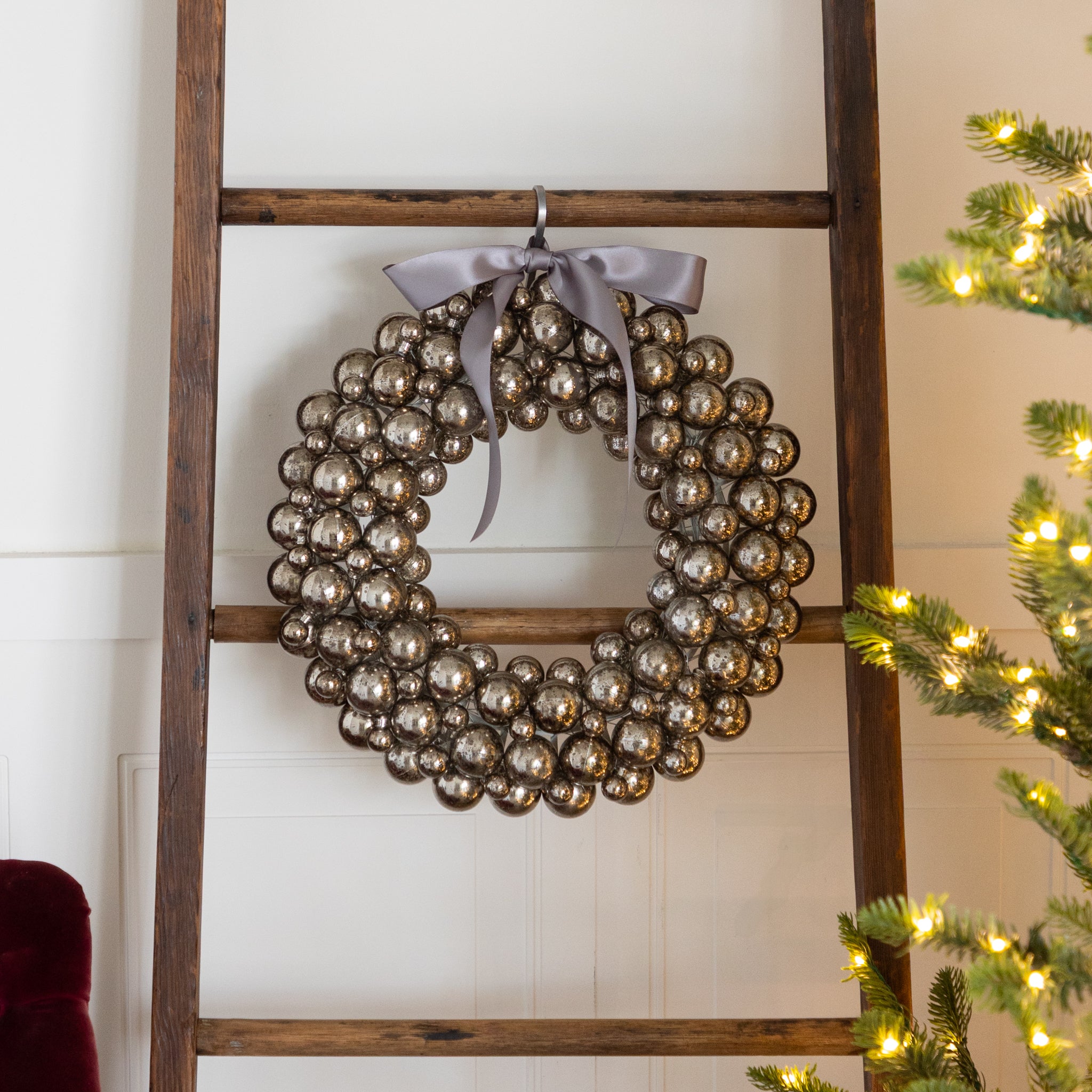 Antique Silver Bubble Wreath with a silver bow hanging on a wooden ladder against a white wall.
