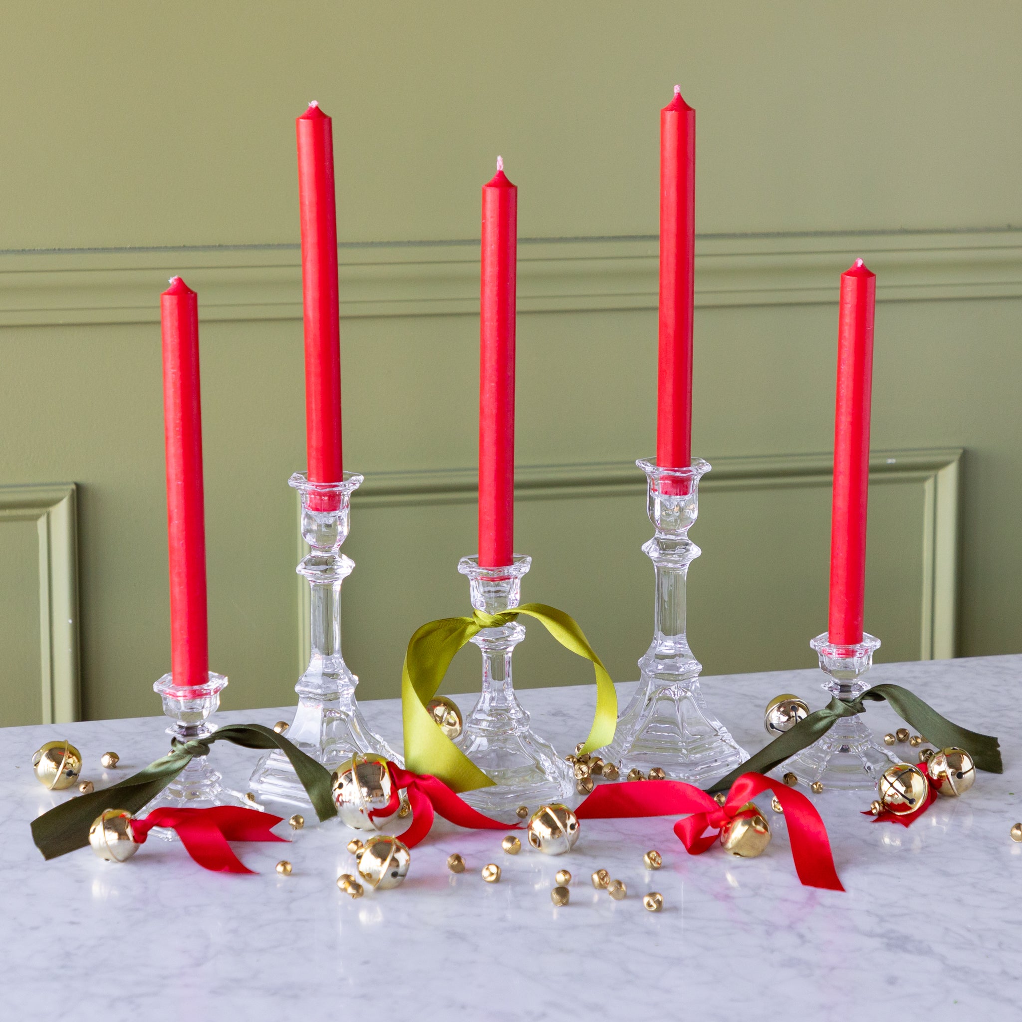 Red candles in glass candlesticks with decorative ribbons and ornaments on a marble surface.