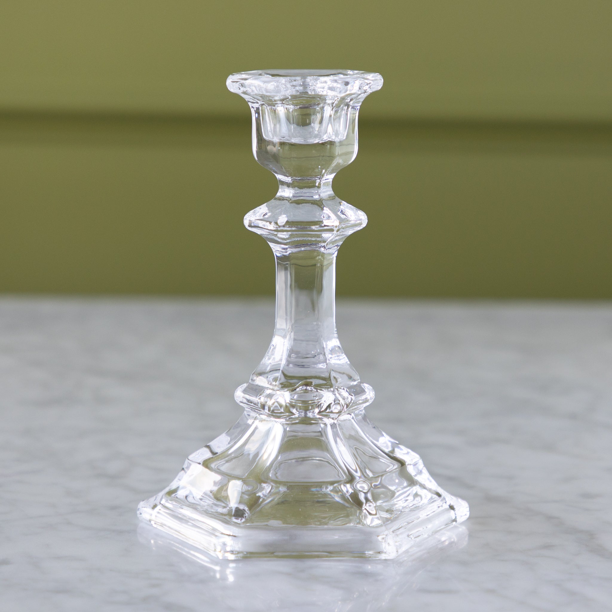 Clear glass candlestick on a marble surface with a green background.