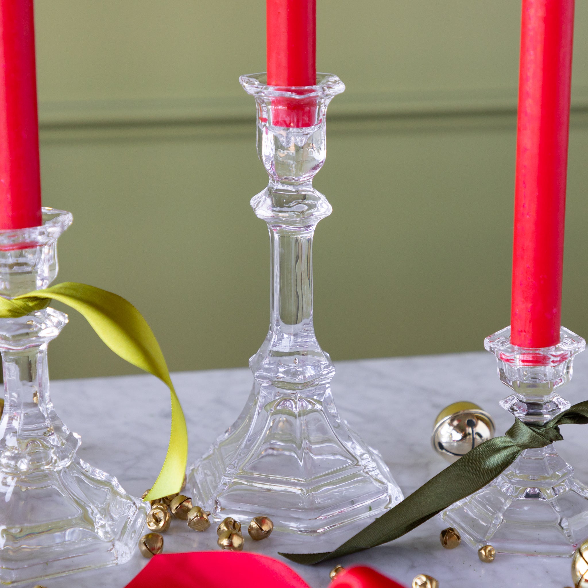 Clear glass candlesticks with red candles on a light surface with green background.