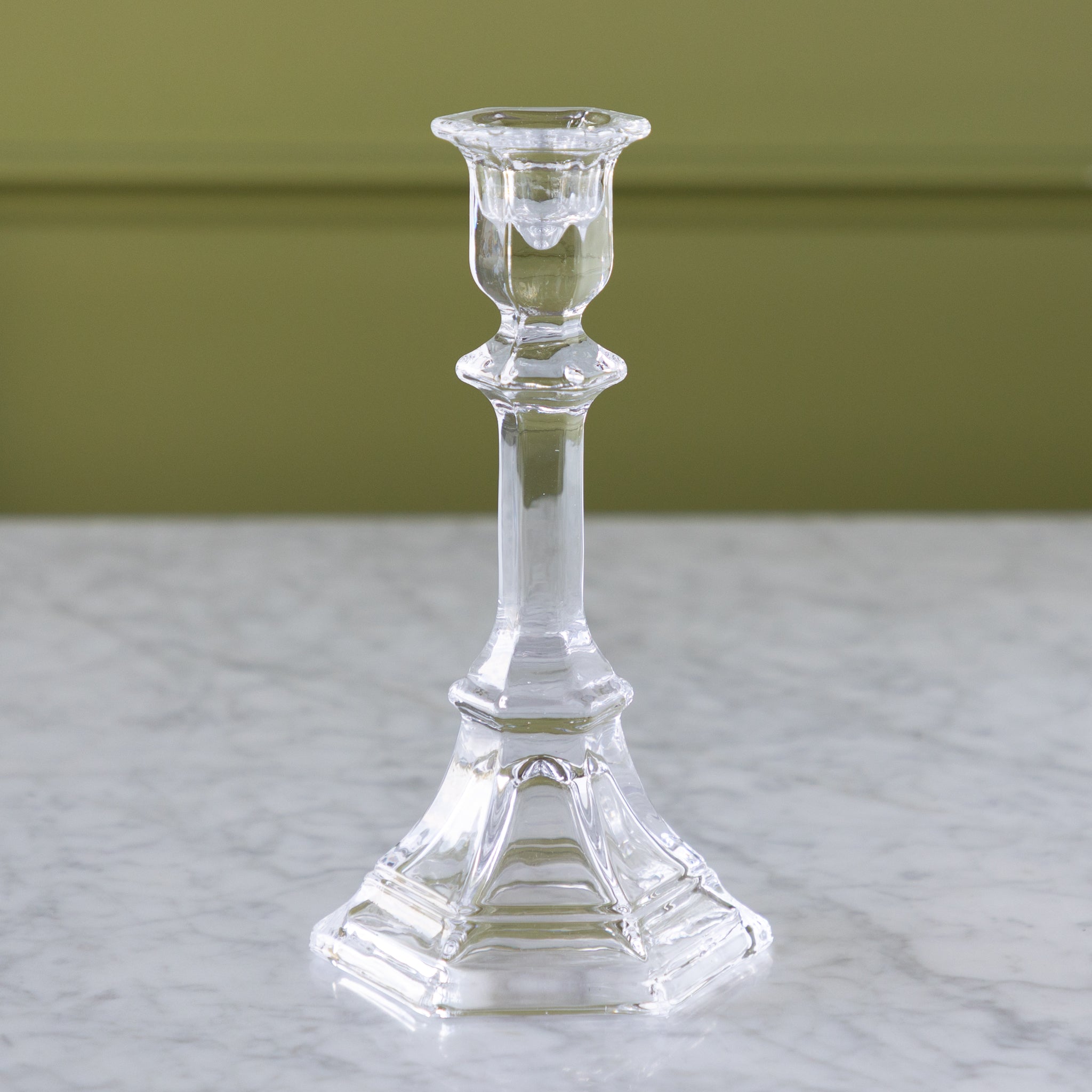 Clear glass candlestick on a marble surface with a green background.