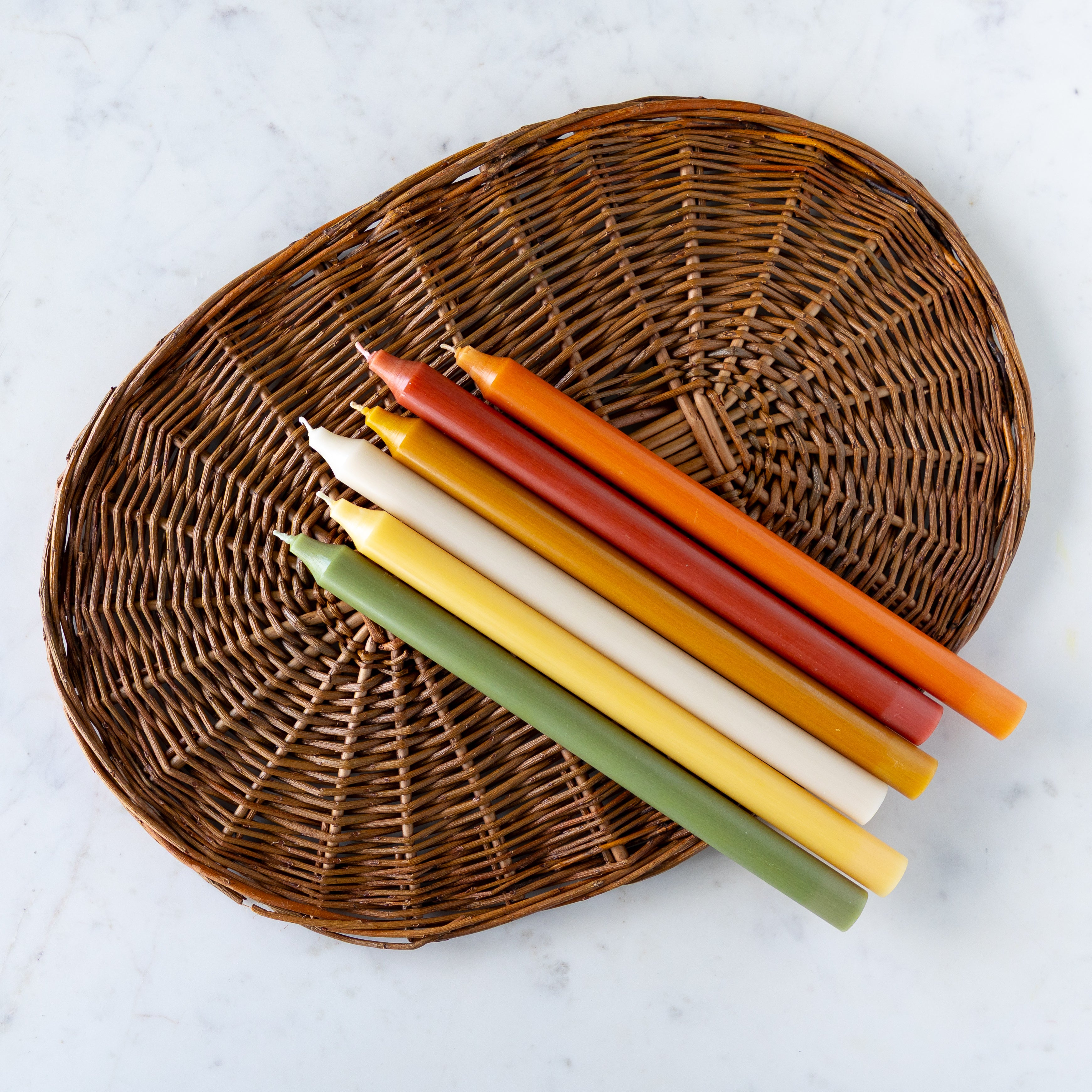 A group of autumn colored taper candles laying on a wicker placemat.