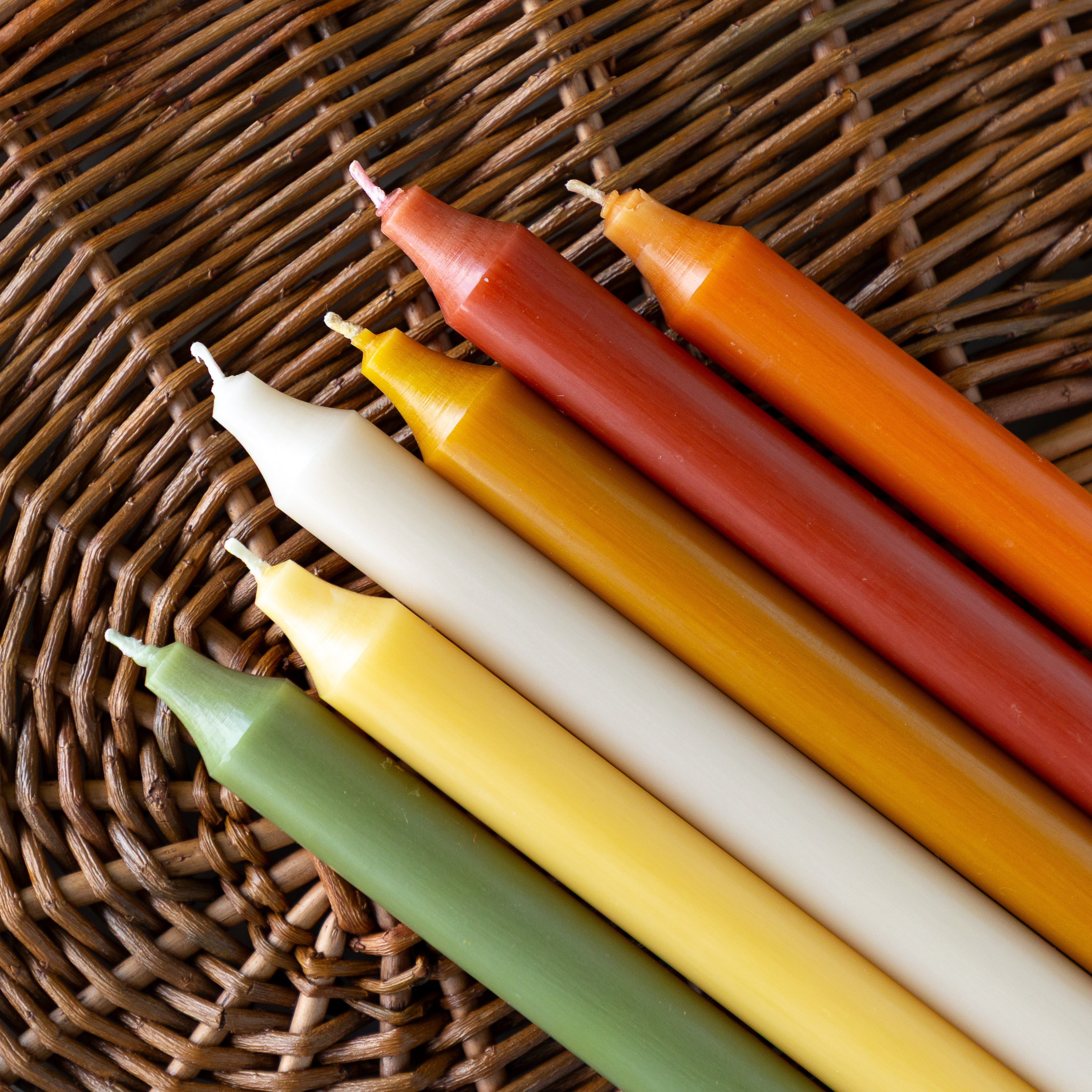 A group of autumn colored taper candles laying on a wicker placemat.