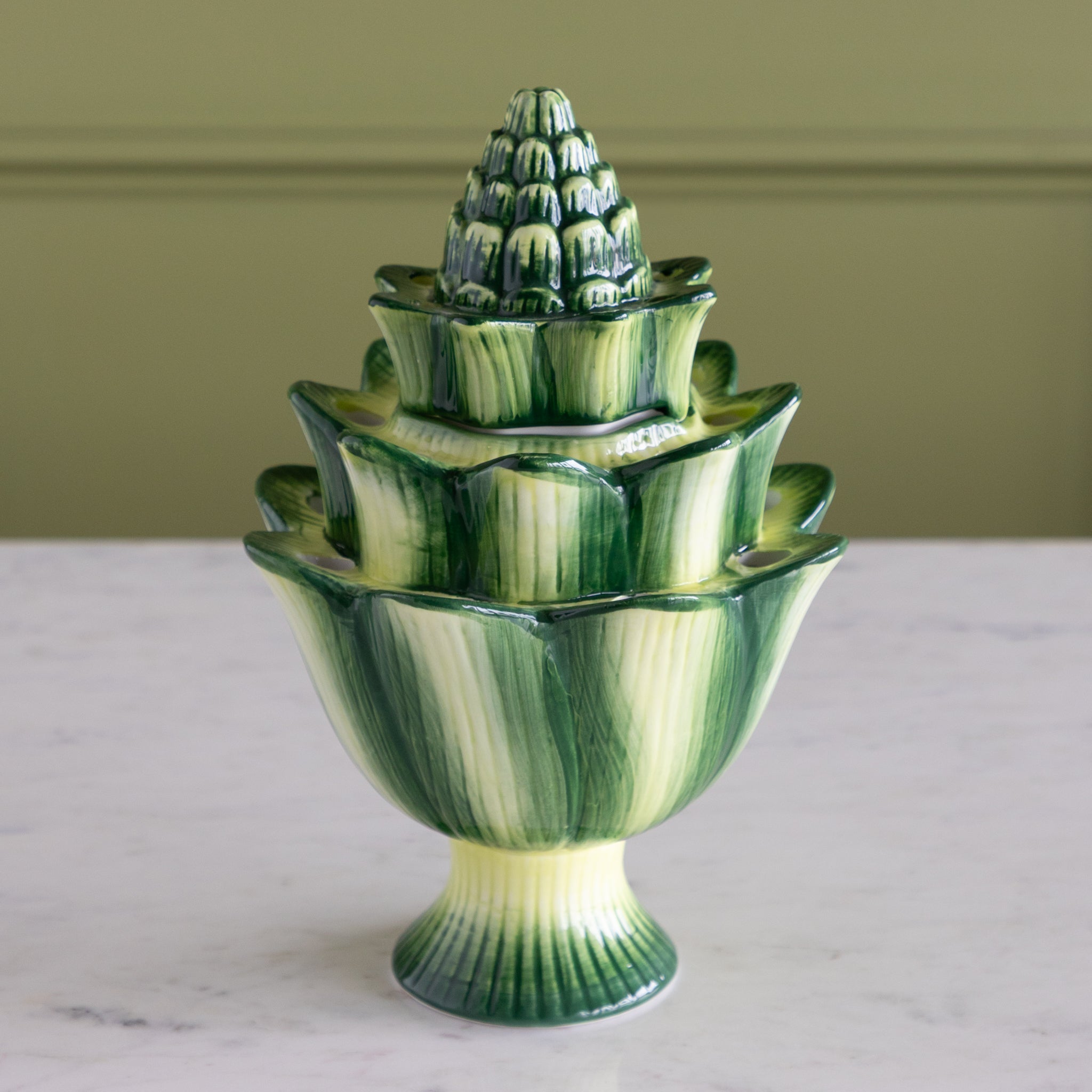 Green ceramic vase with a textured design on a white surface and green background.