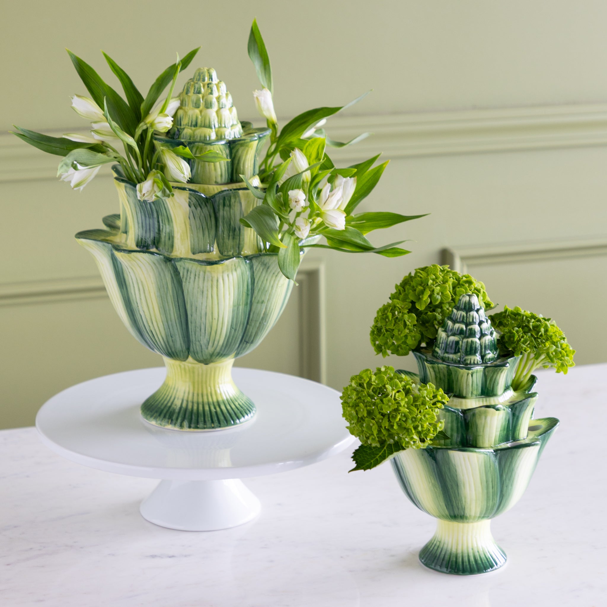 Decorative green and white ceramic vases with floral arrangements on a white surface.