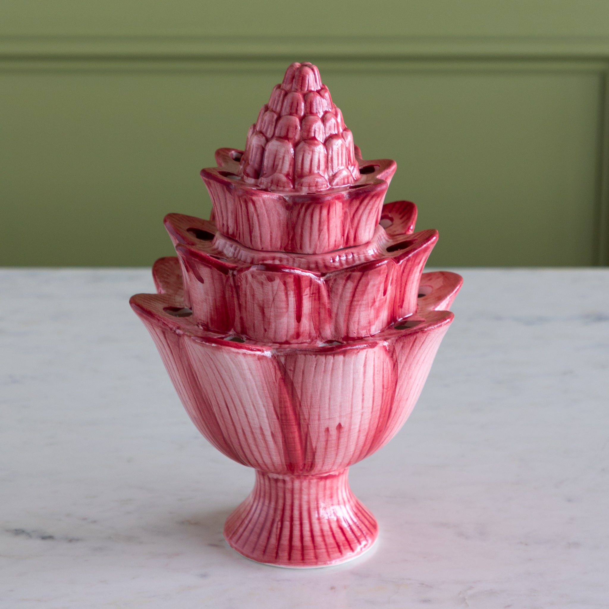 Pink ceramic tiered vase on a marble surface with a green wall background.