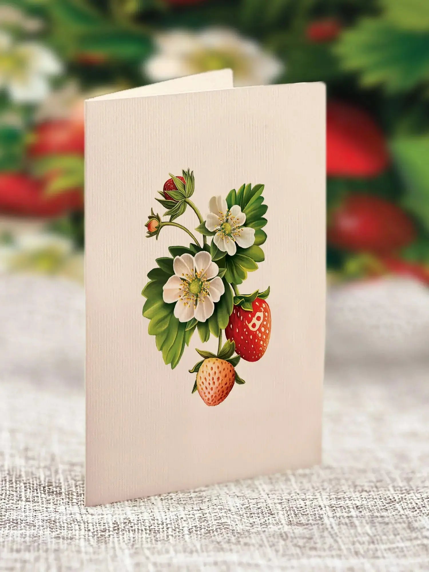Card with strawberry illustration on a textured surface with blurred strawberries in the background