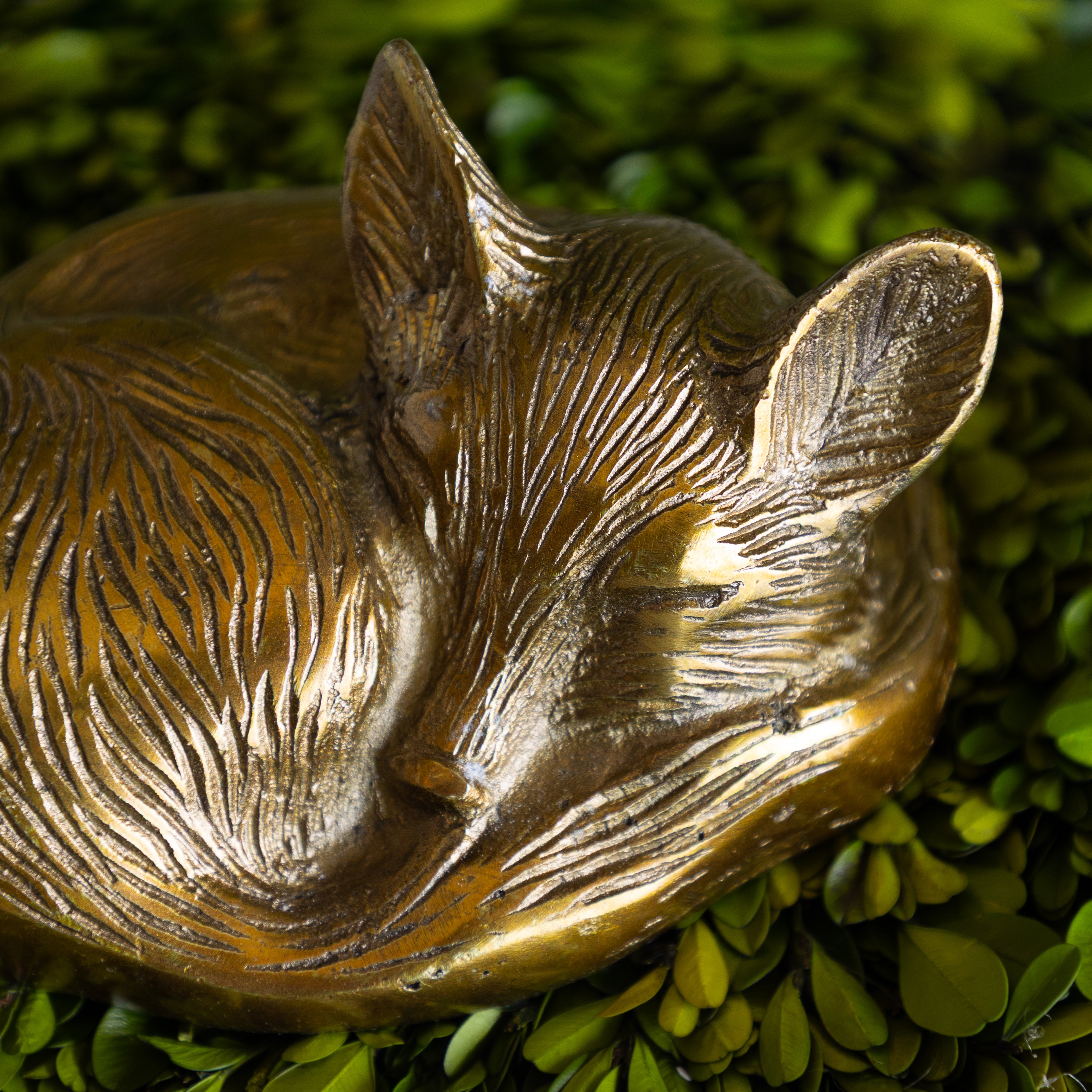 Bronze fox figurine on a green leafy background