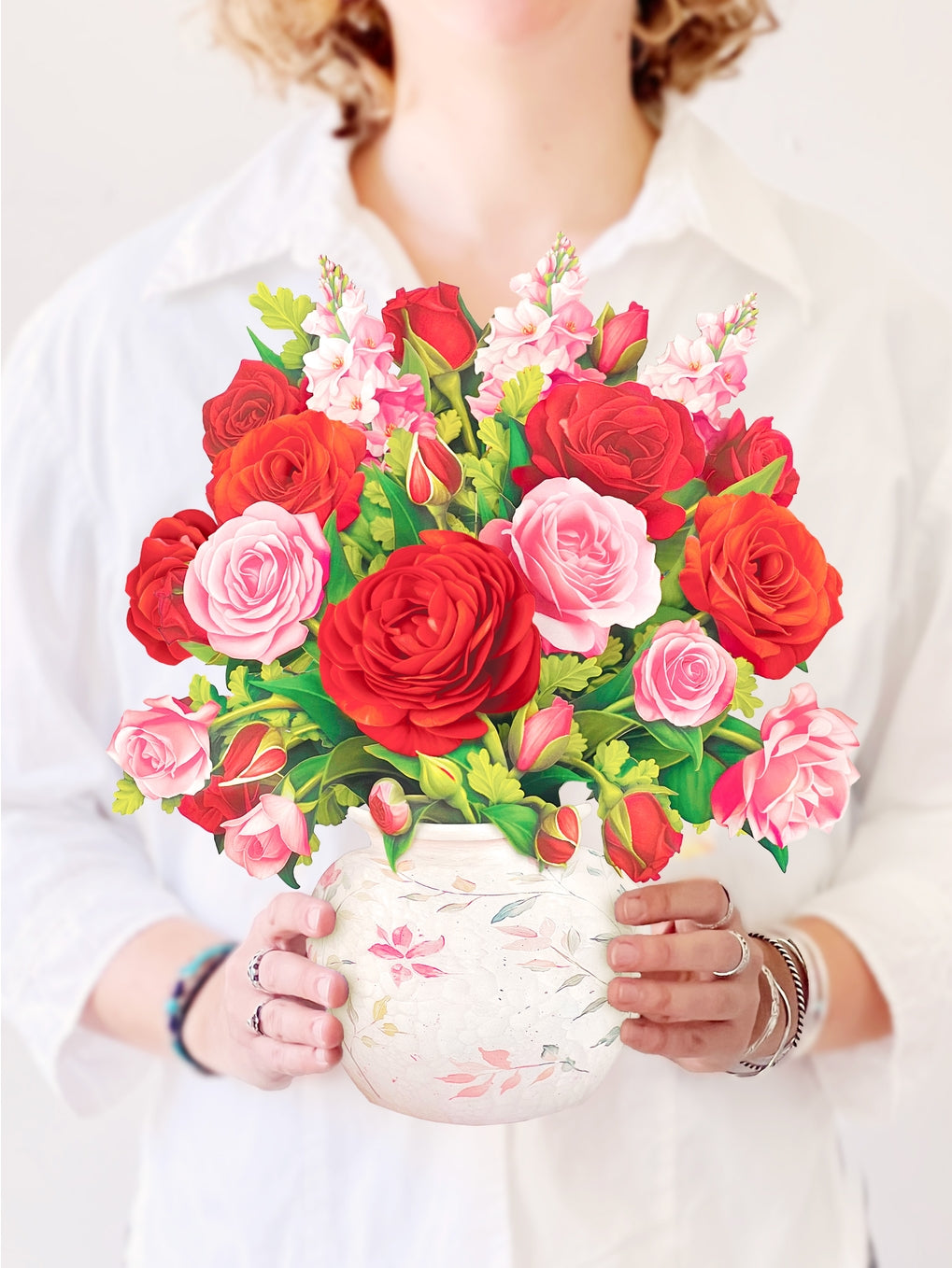Person holding a bouquet of red and pink roses in a decorative vase.