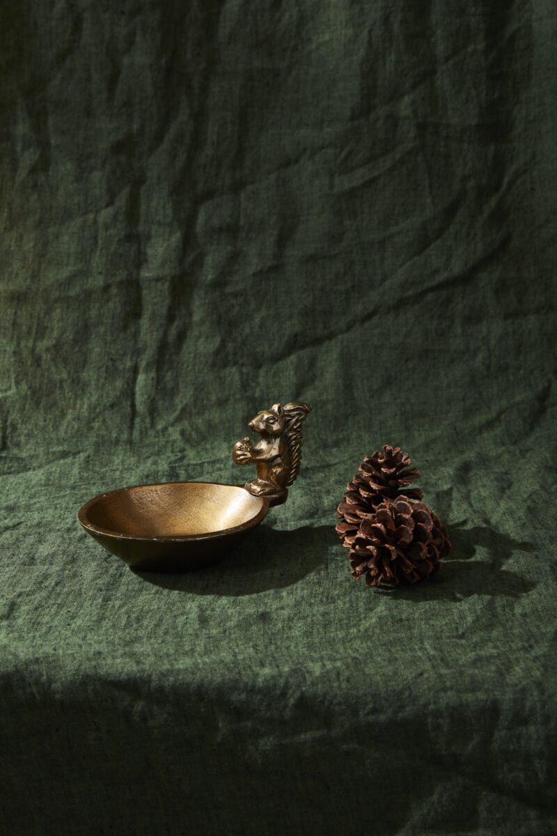 Bronze squirrel-themed bowl with a pine cone on a green fabric background