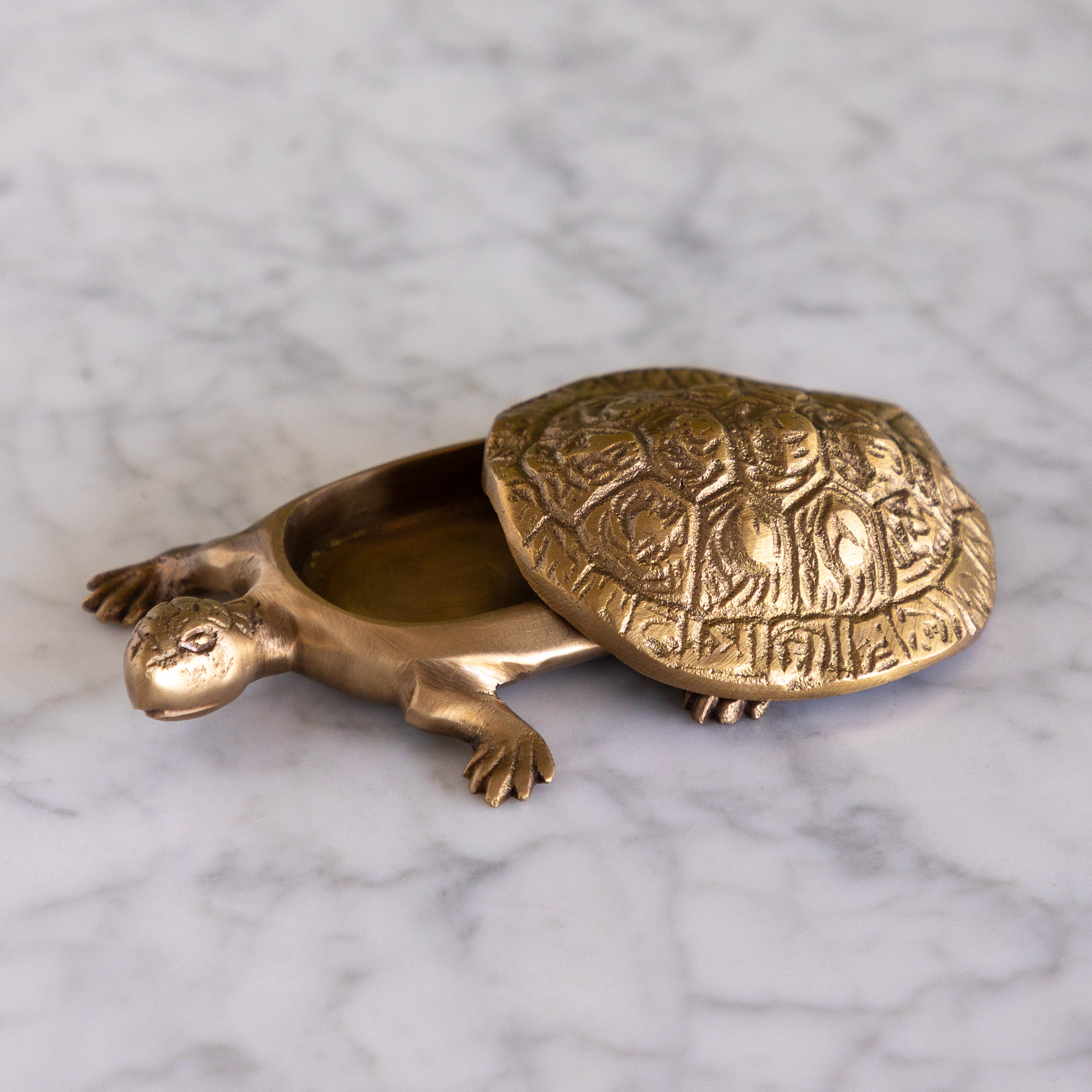 A brass turtle-shaped container with an open shell, resting on a white marble surface.