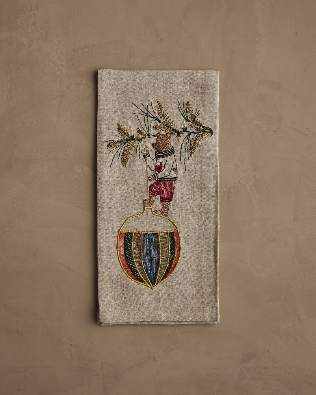 Decorative napkin with embroidered design of a bear holding a bottle against a beige background