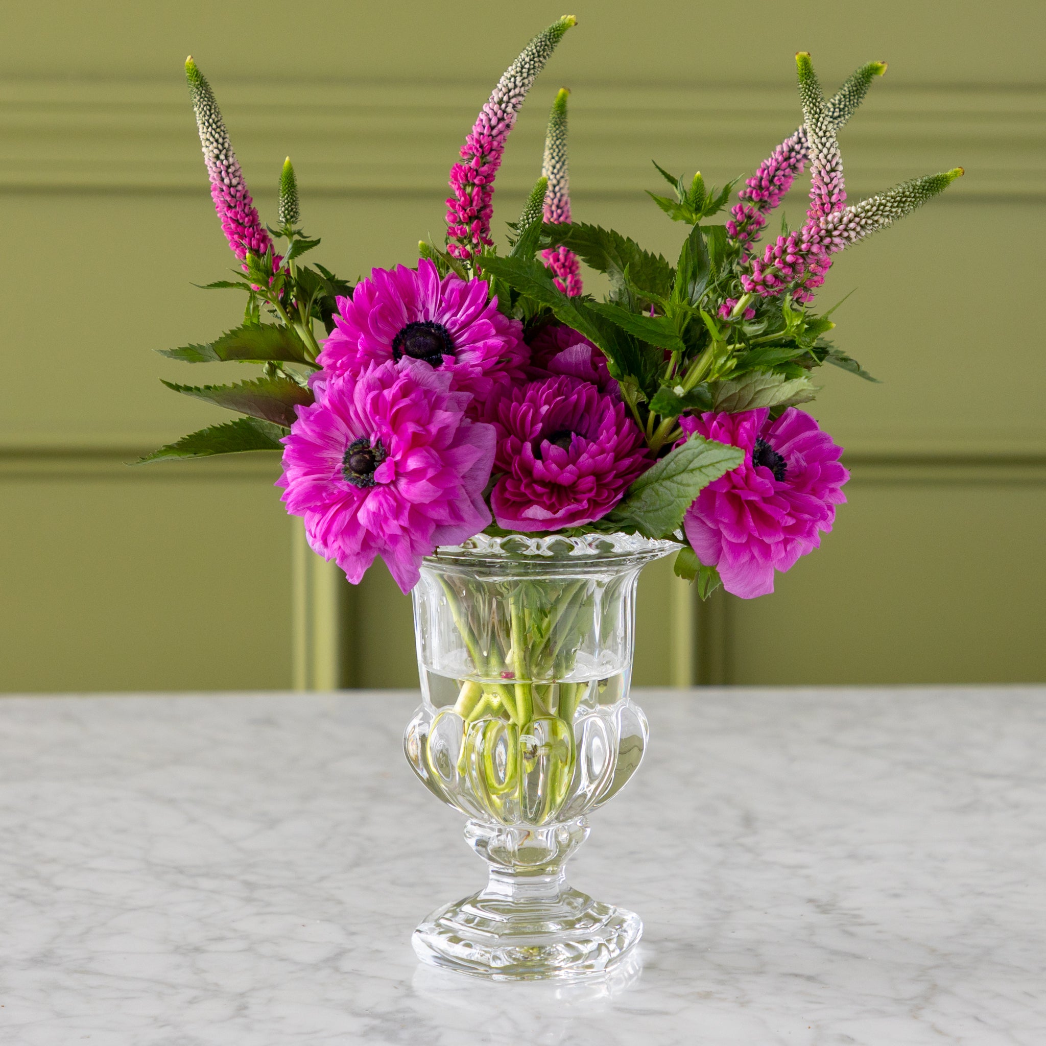Clear glass vase with pink flowers on a marble surface and green background