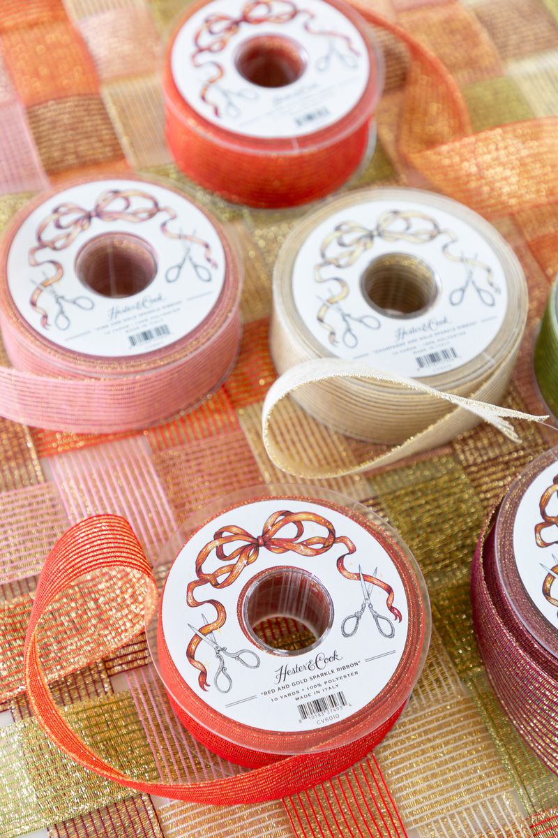 Several spools of sparkly ribbon in various colors unraveled on a surface of woven sparkle ribbon.