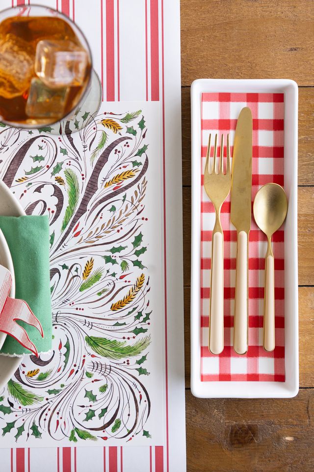 Set of gold cutlery on a red and white checkered tray with a decorative table mat and glass of iced tea.