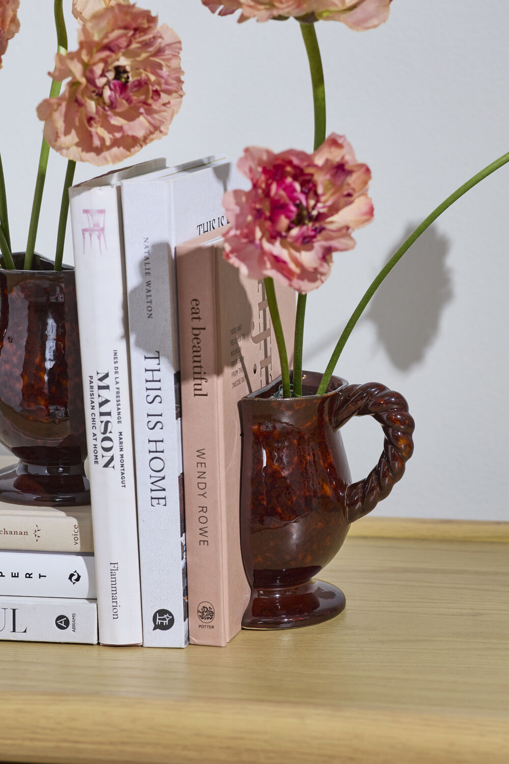 Decorative setup with books and a vase containing pink flowers on a wooden surface.