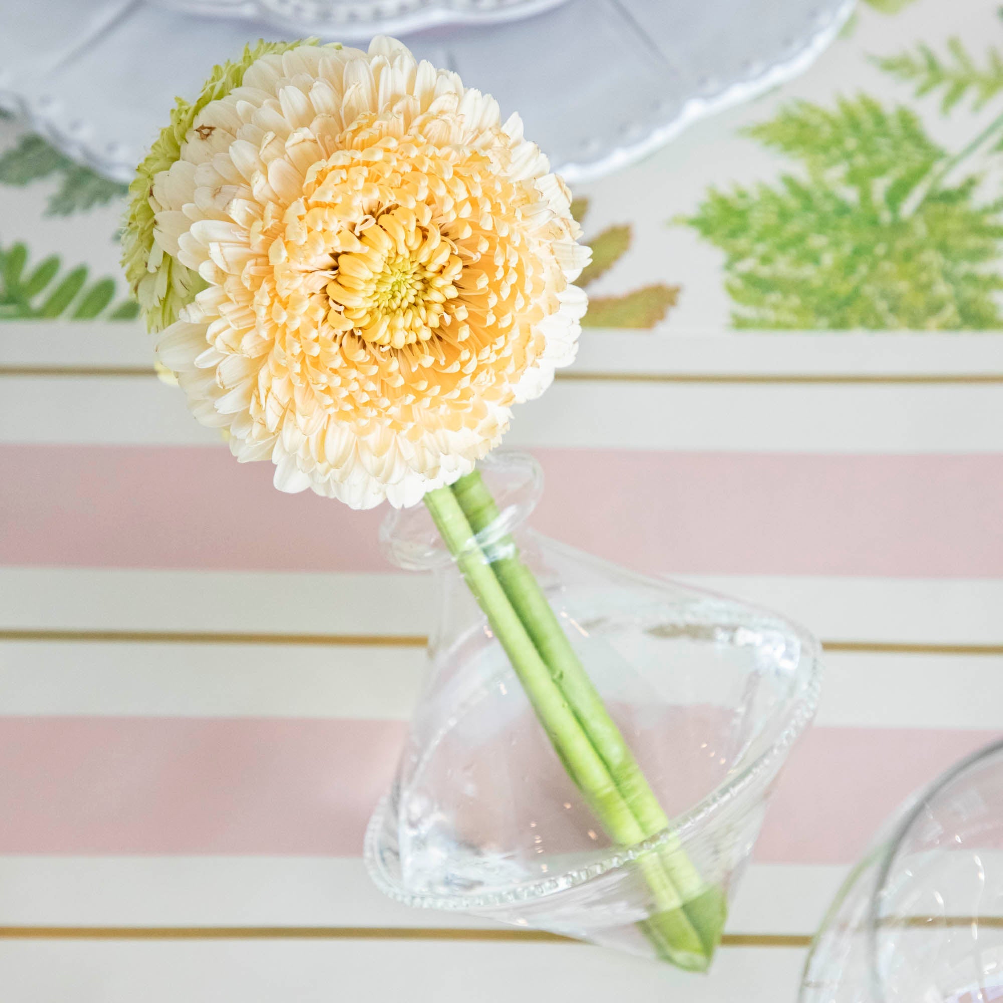 A Qualia mouth blown clear vase with a small bouquet of yellow flowers on a table.