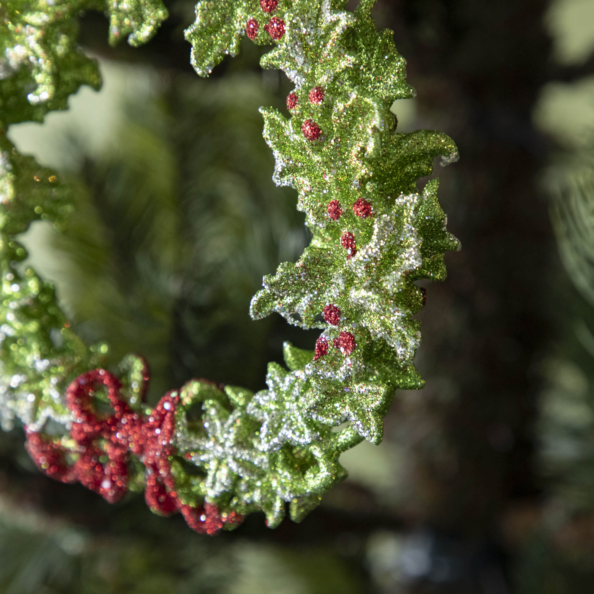 A close up of the green wreath ornament showing its silver accents, bright red berries and a red bow.