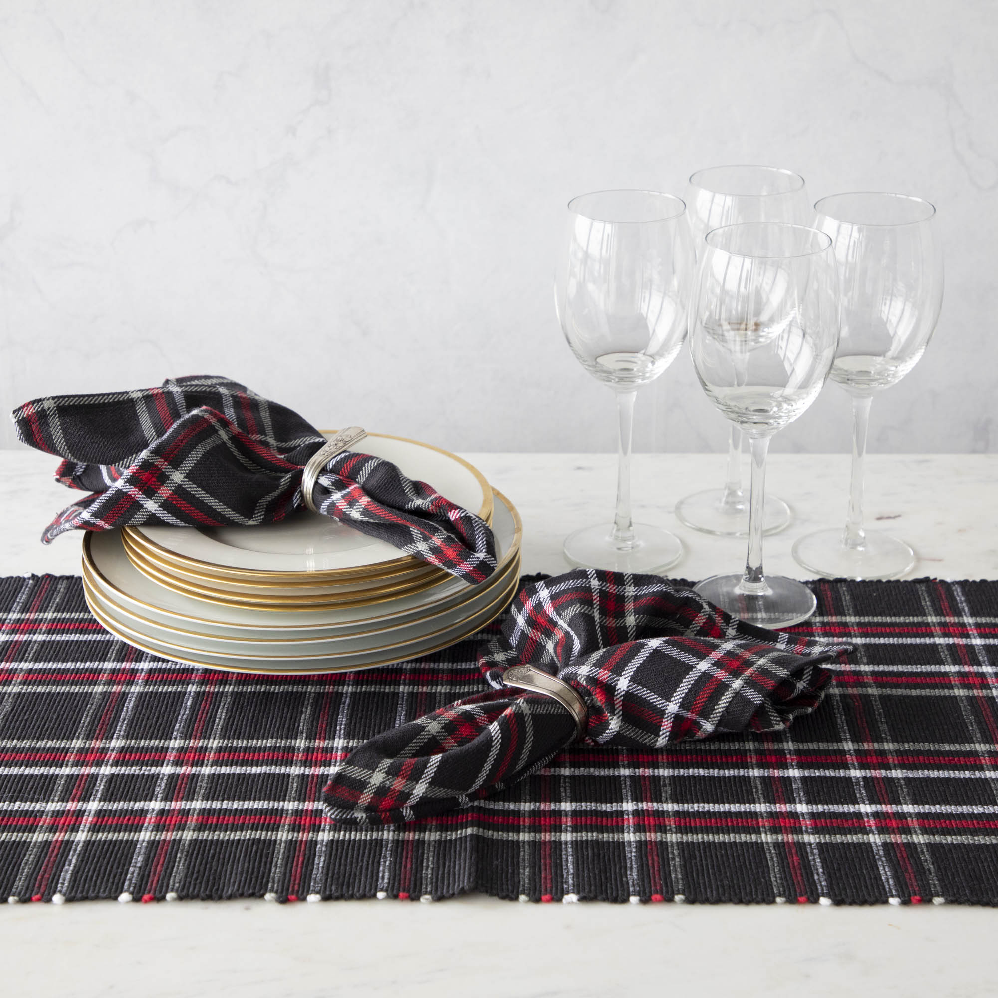 Two red plaid cotton napkins in napkin rings, displayed on a table with a matching plaid runner.