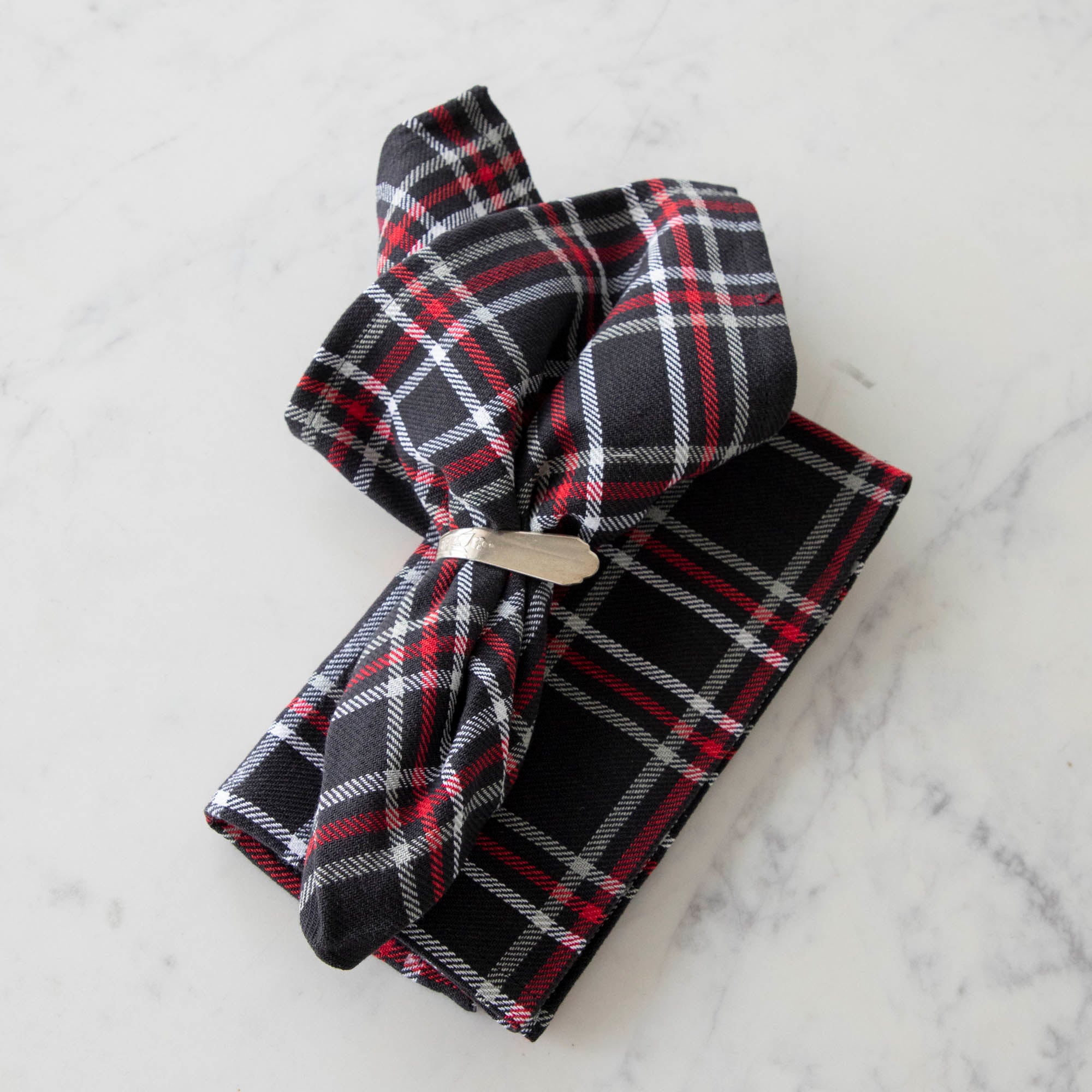 Two black plaid cotton napkins, one folded and one in a napkin ring, displayed on a white surface.