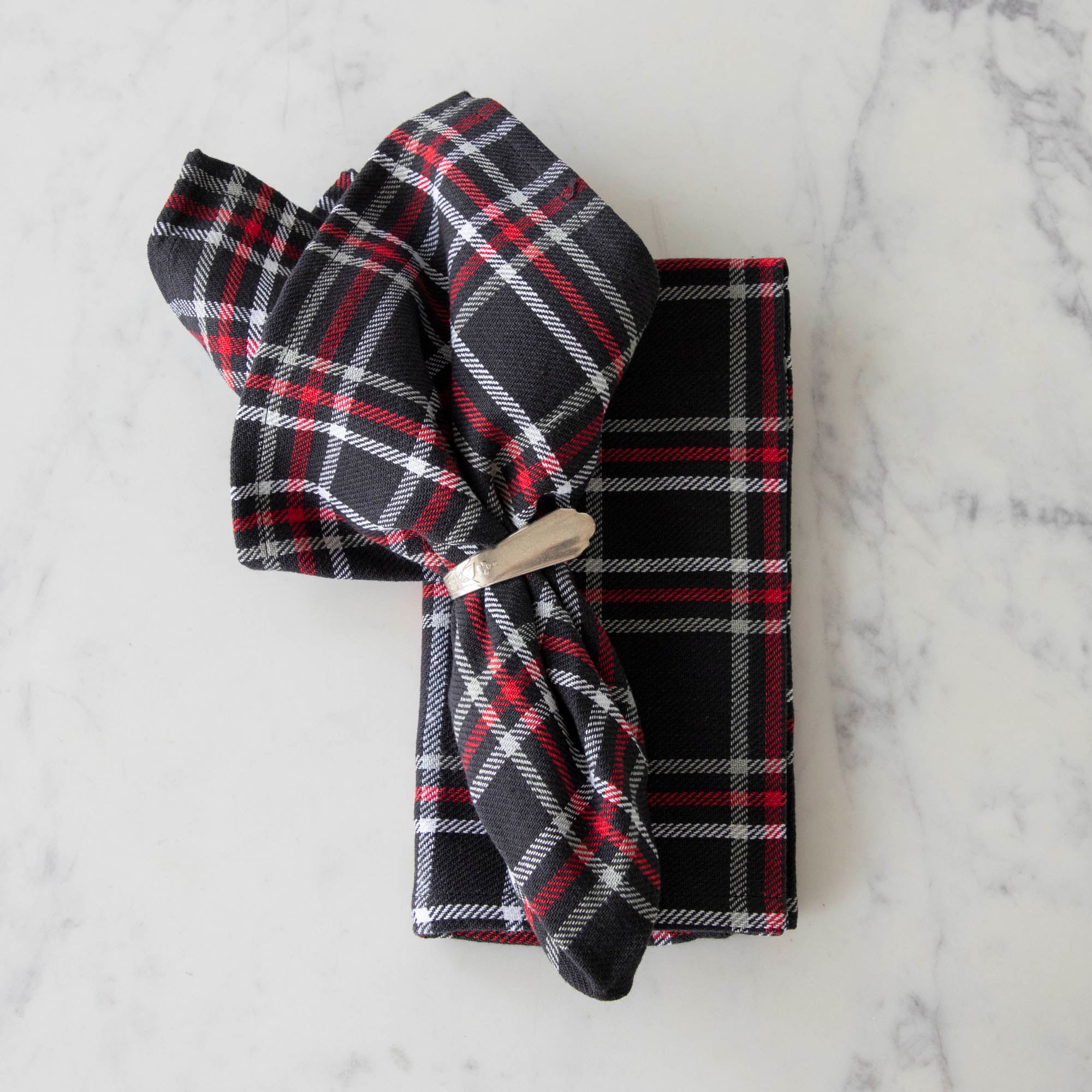 Two black plaid cotton napkins, one folded and one in a napkin ring, displayed on a white surface.