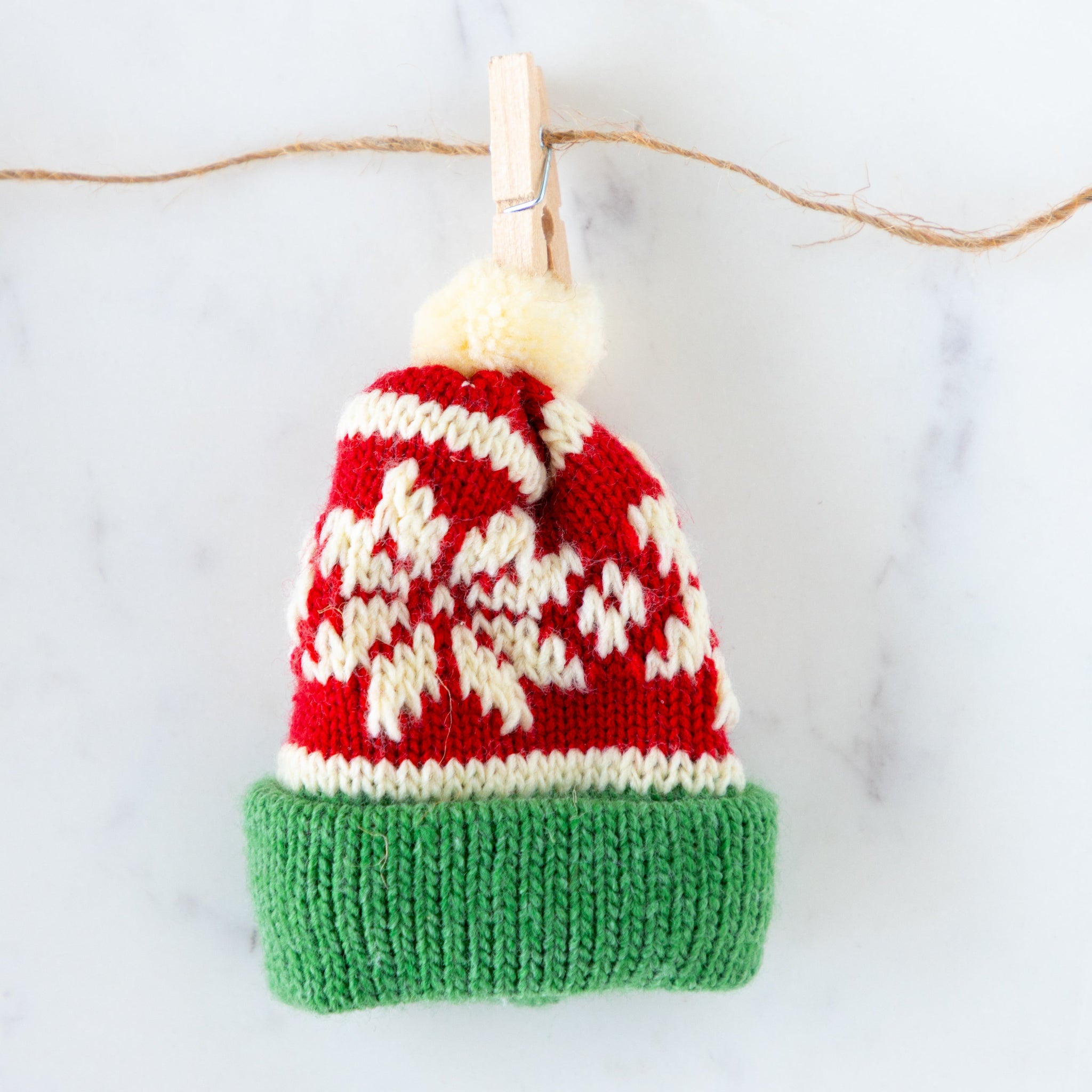 Knitted hat with red, white, and green colors hanging on a clothesline.