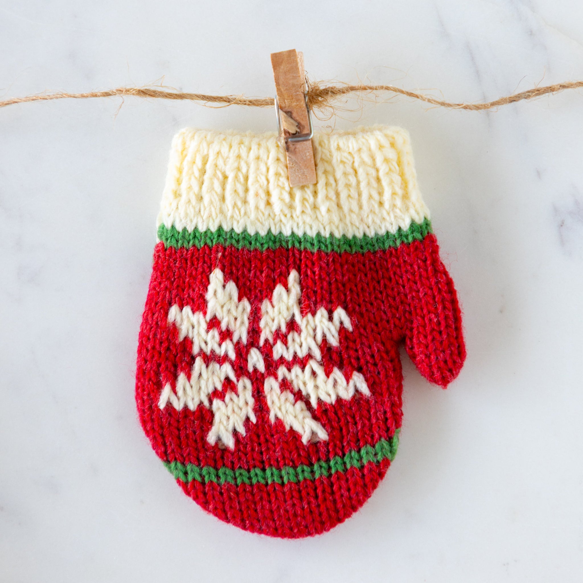 Knitted red and white mitten with a snowflake design, hanging on a line.