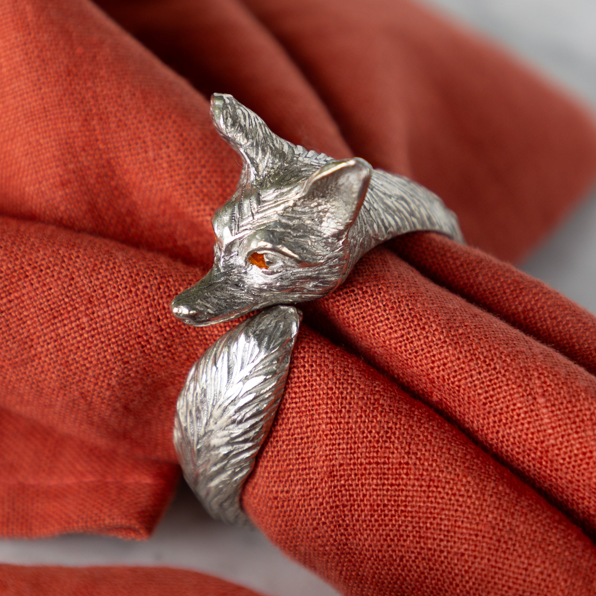 Silver fox-shaped ring around an orange napkin.
