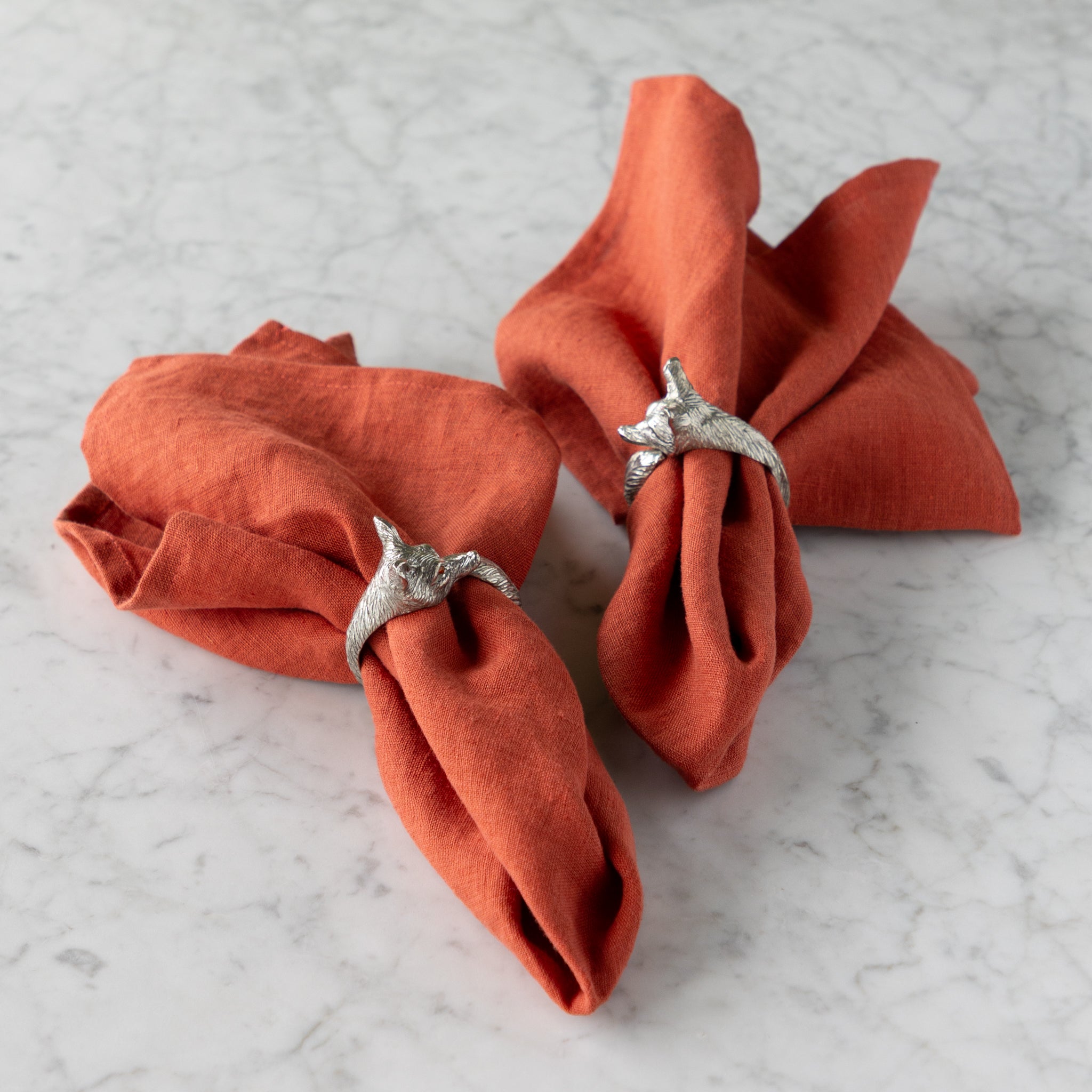 Two orange napkins with fox napkin rings on a marble surface.