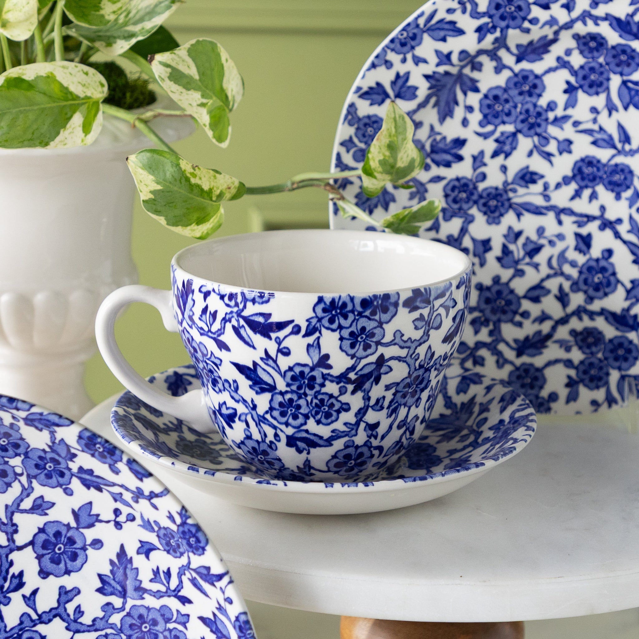 Burleigh Blue Arden teacup and saucer with a green plant in the background.