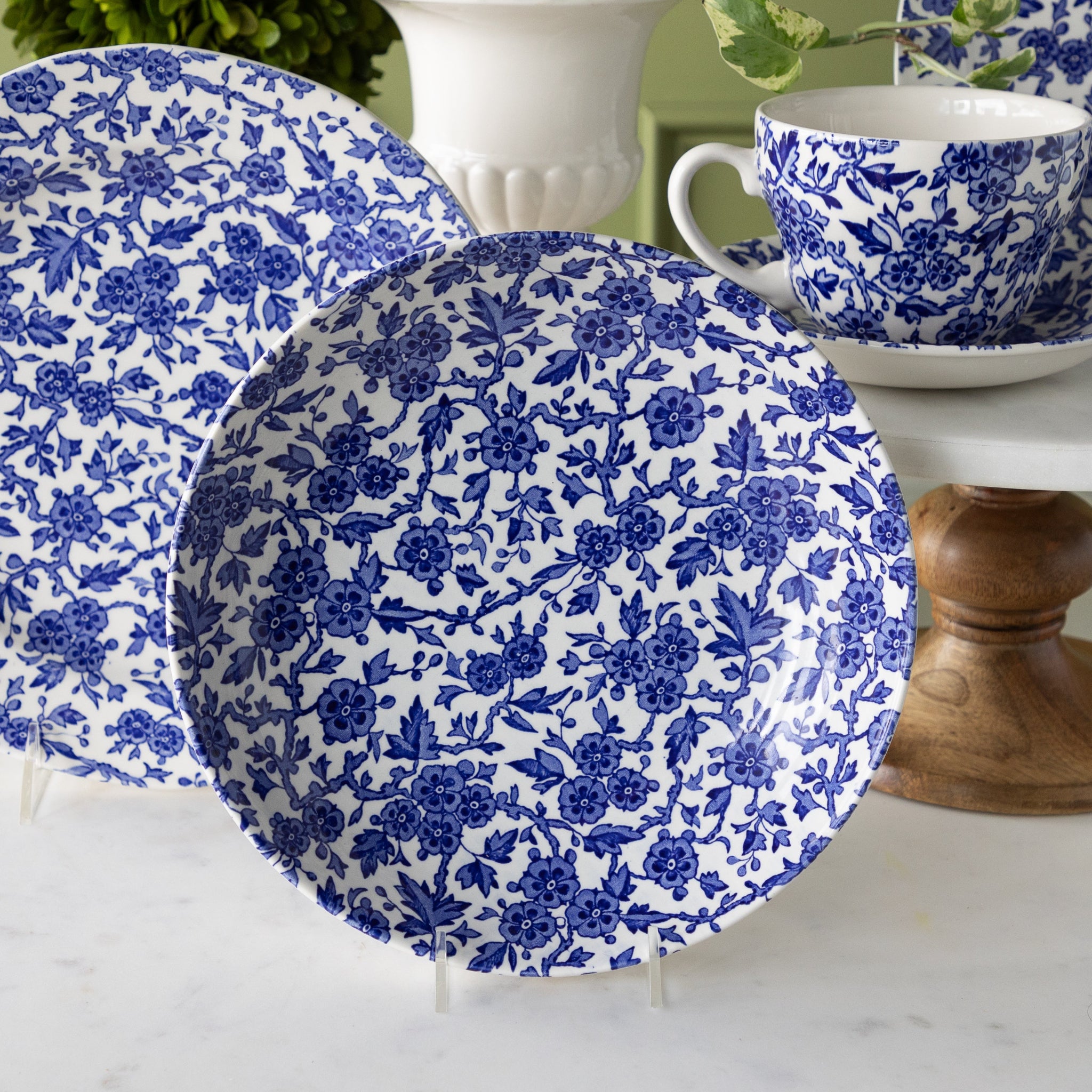 Burleigh Blue Arden Pasta Bowl propped on a stand in front of a teacup and saucer and dinner plate.