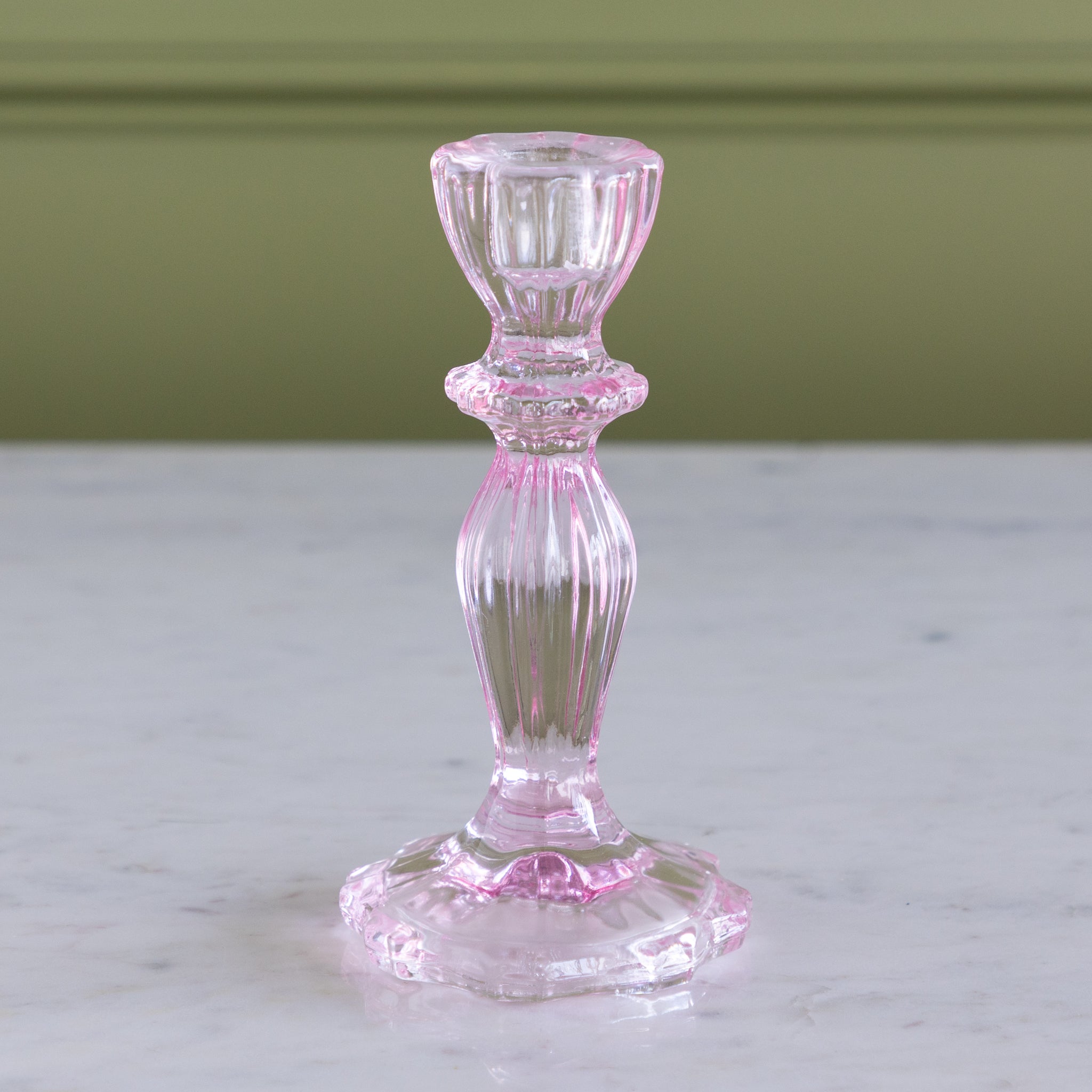 Pink glass candlestick holder on a marble surface with a green wall background.