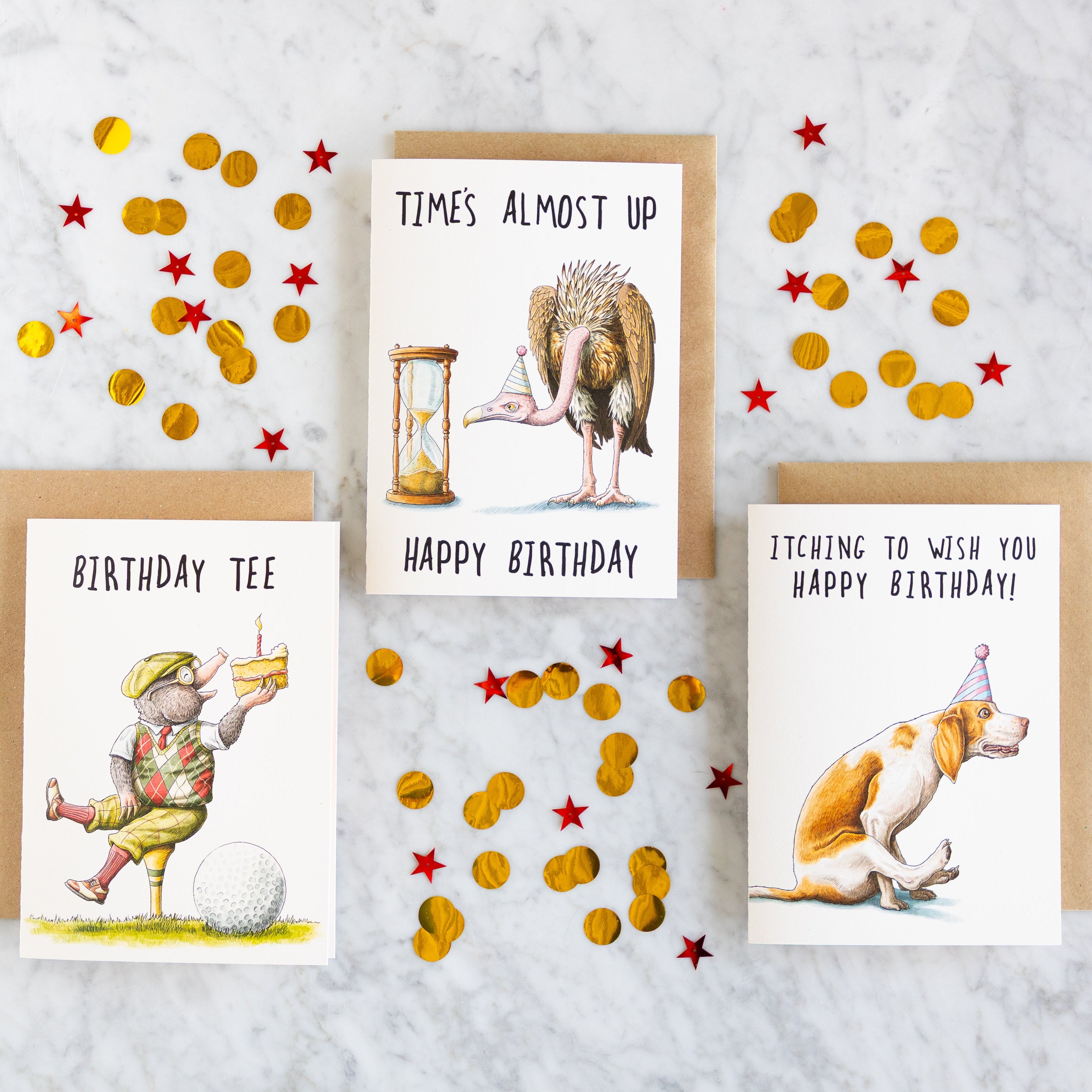 Three Bewilderbeest birthday cards with illustrations and text on a marble table with confetti.