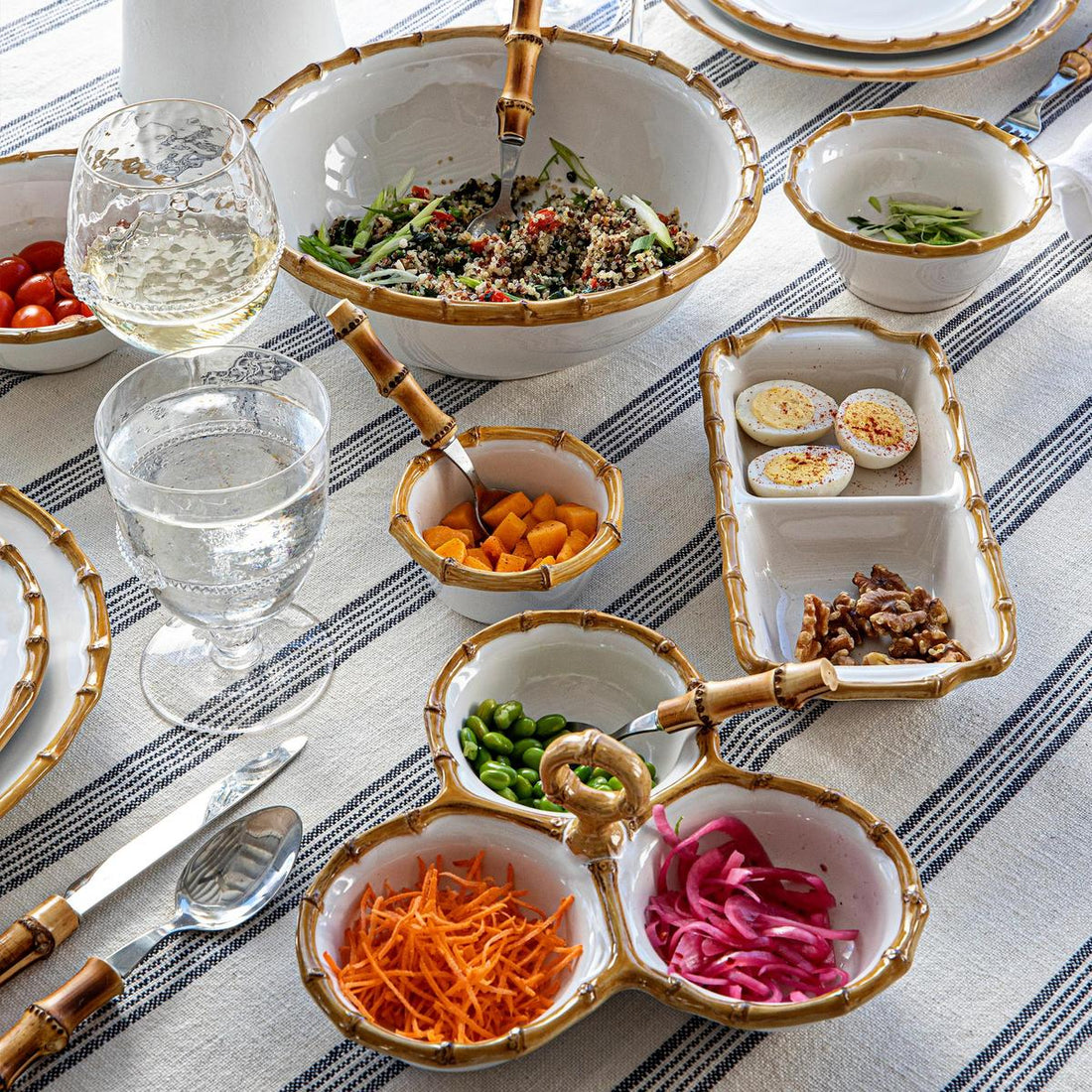 Elegant table setting featuring a variety of salads and appetizers with gold-trimmed, hand-painted Juliska ceramic dinnerware and glassware, along with Juliska Classic Natural Bamboo Serving Pieces.