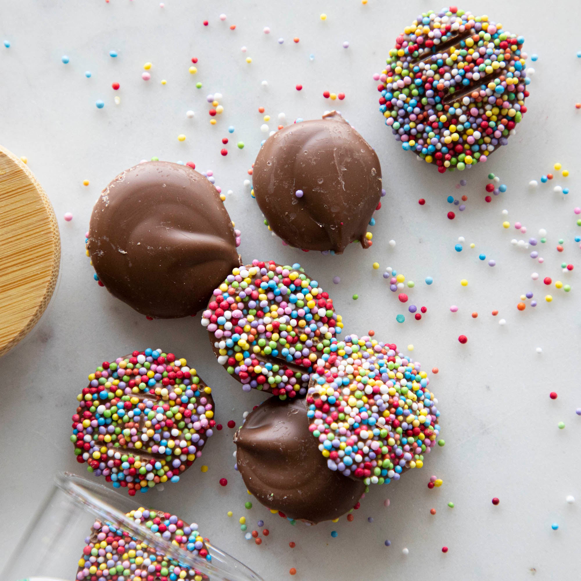 A group of Hester & Cook Chocolate Buttons with sprinkles and natural nonpareils on a table.