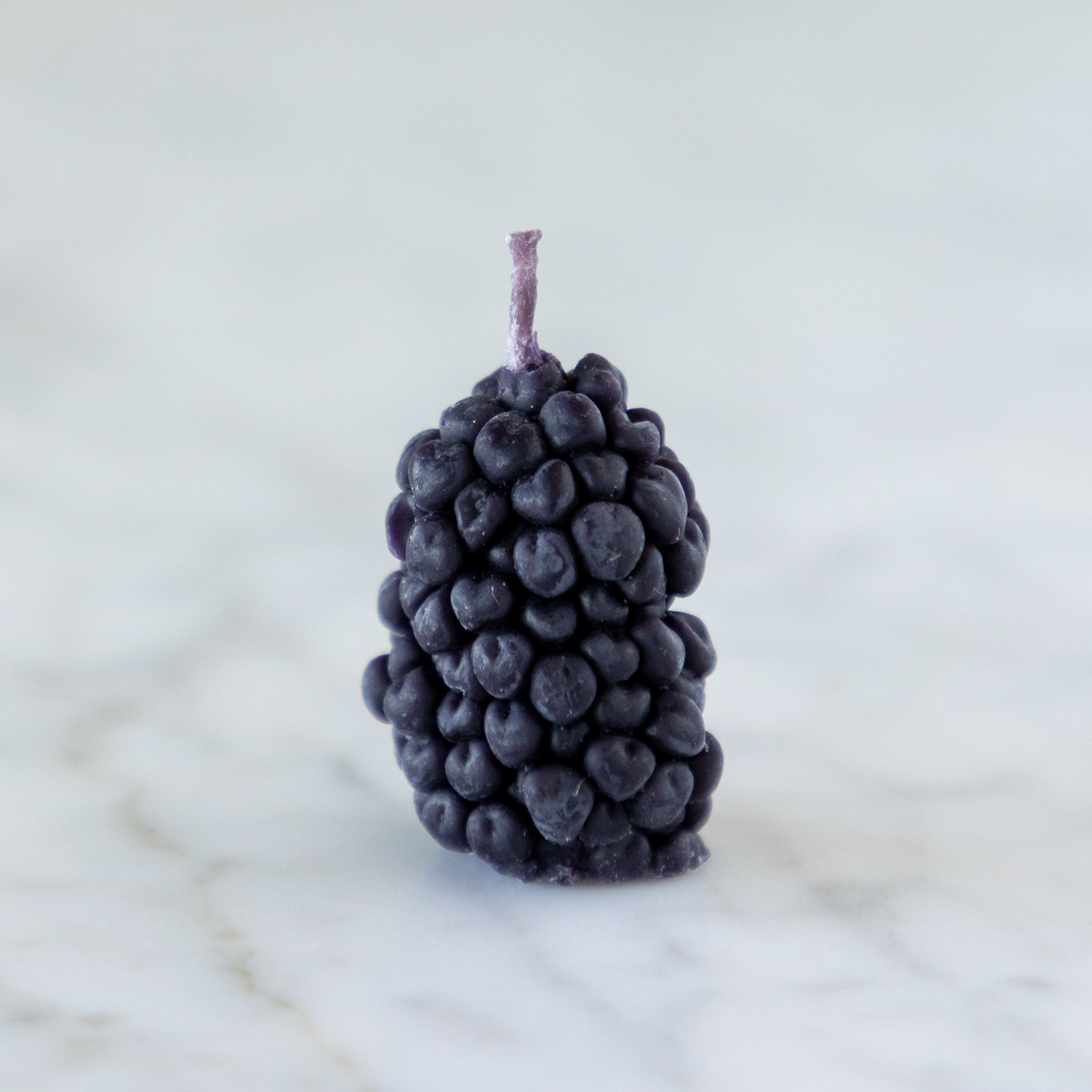 A single, blackberry-shaped candle with a purple stem on a marble surface.