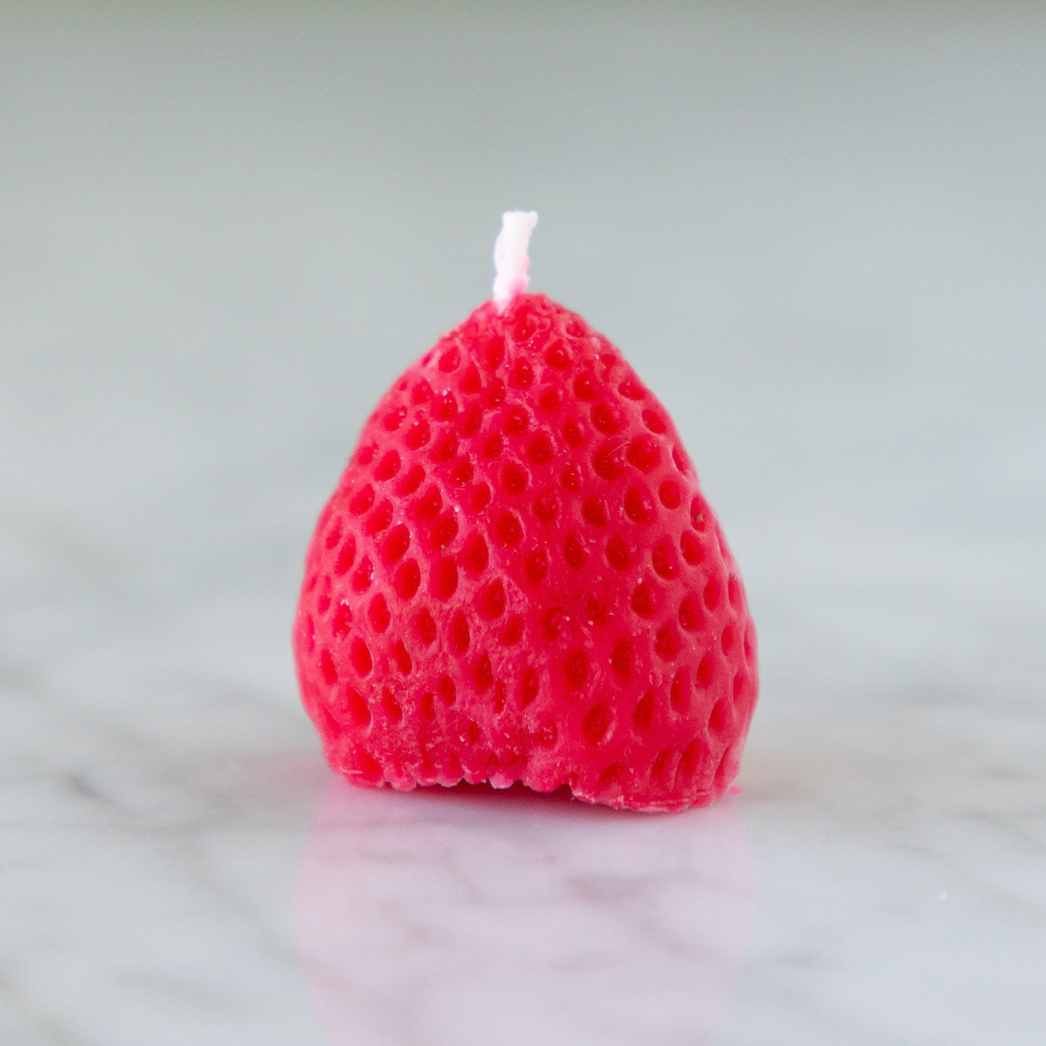 A strawberry shaped candle on a marble surface.