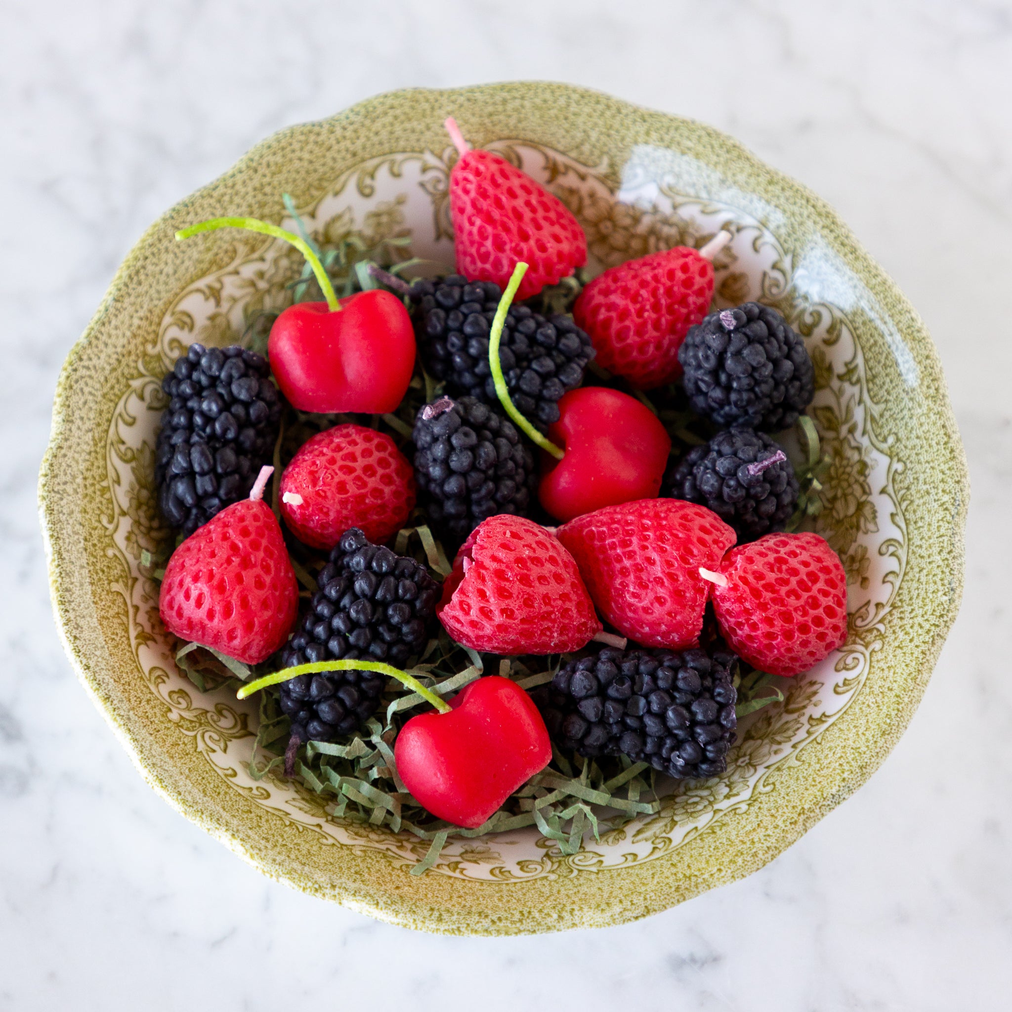 A decorative bowl filled with strawberry, blackberry and cherry shaped candles.