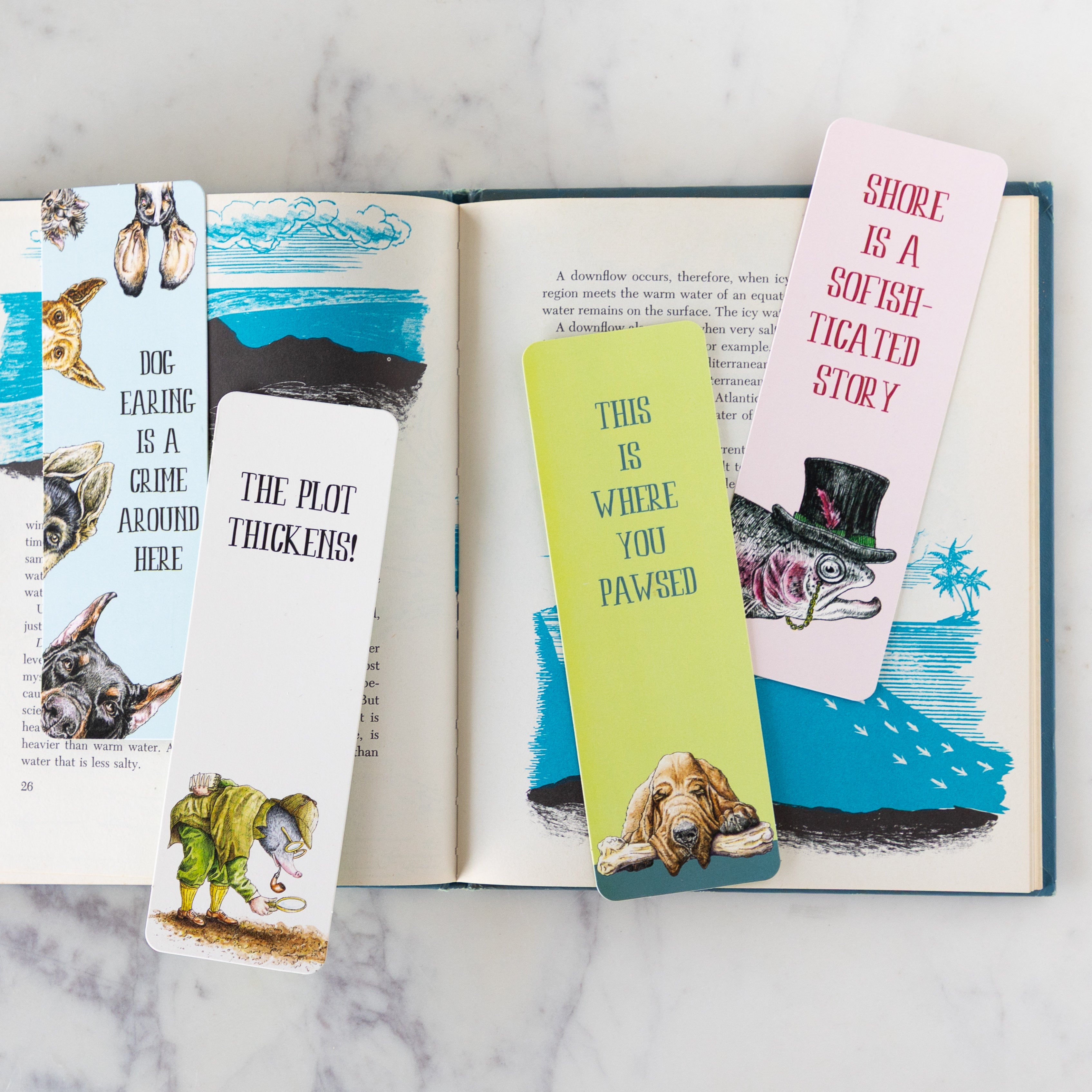 An open book on a table with four Bewilderbeest Bookmarks on top.