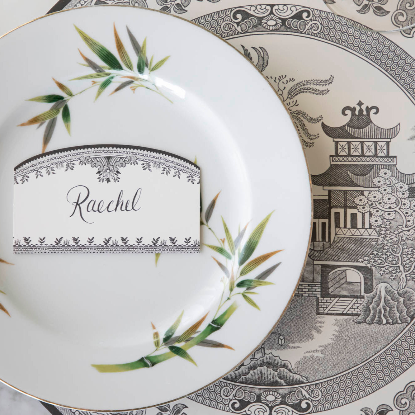 Black Willow Place Card with "Raechel" written on it, resting on a dinner plate on top of the Die-cut Black Willow Placemat.