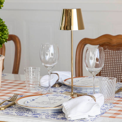 An elegantly set dining table with a modern Zafferano glossy gold cordless lamp, matching dinnerware, and glassware.